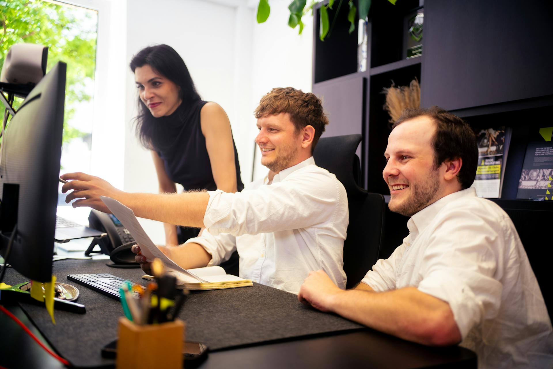 Three colleagues collaborating on a project in a bright, modern office with technology at hand.