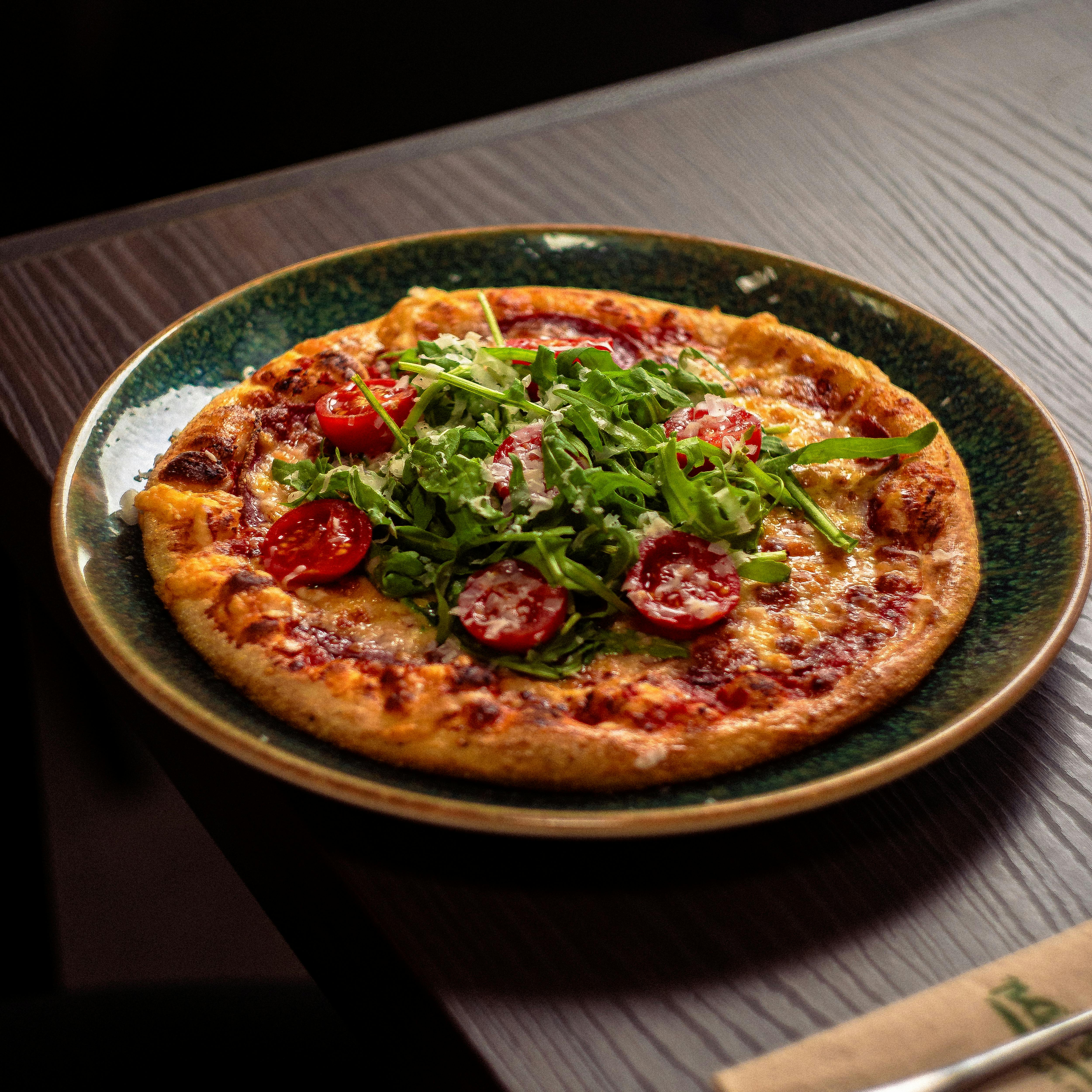 Close-up of a pizza topped with fresh arugula and cherry tomatoes in a restaurant setting.