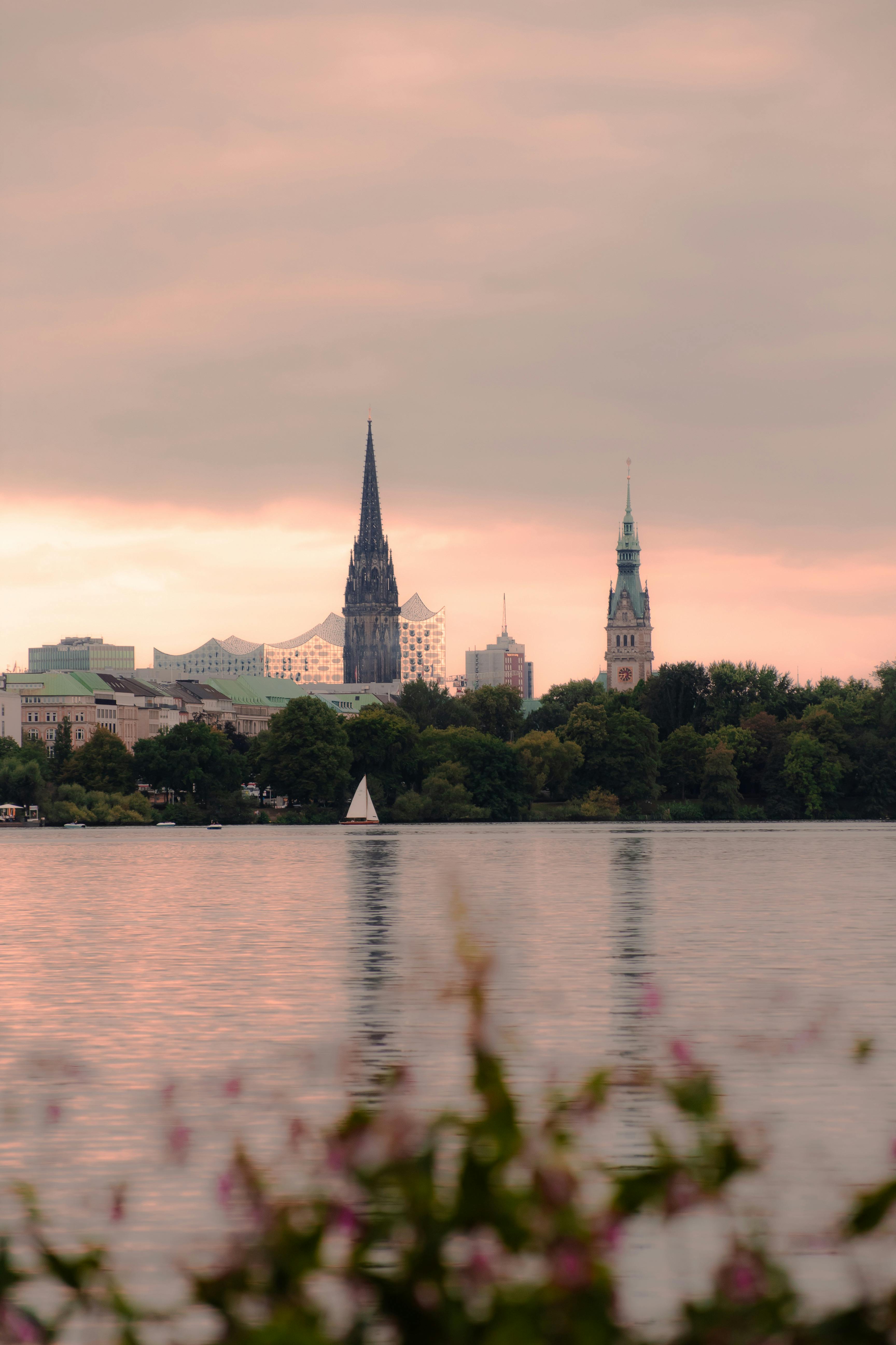 Hamburg cityscape with iconic spires reflecting on the river during sunset.