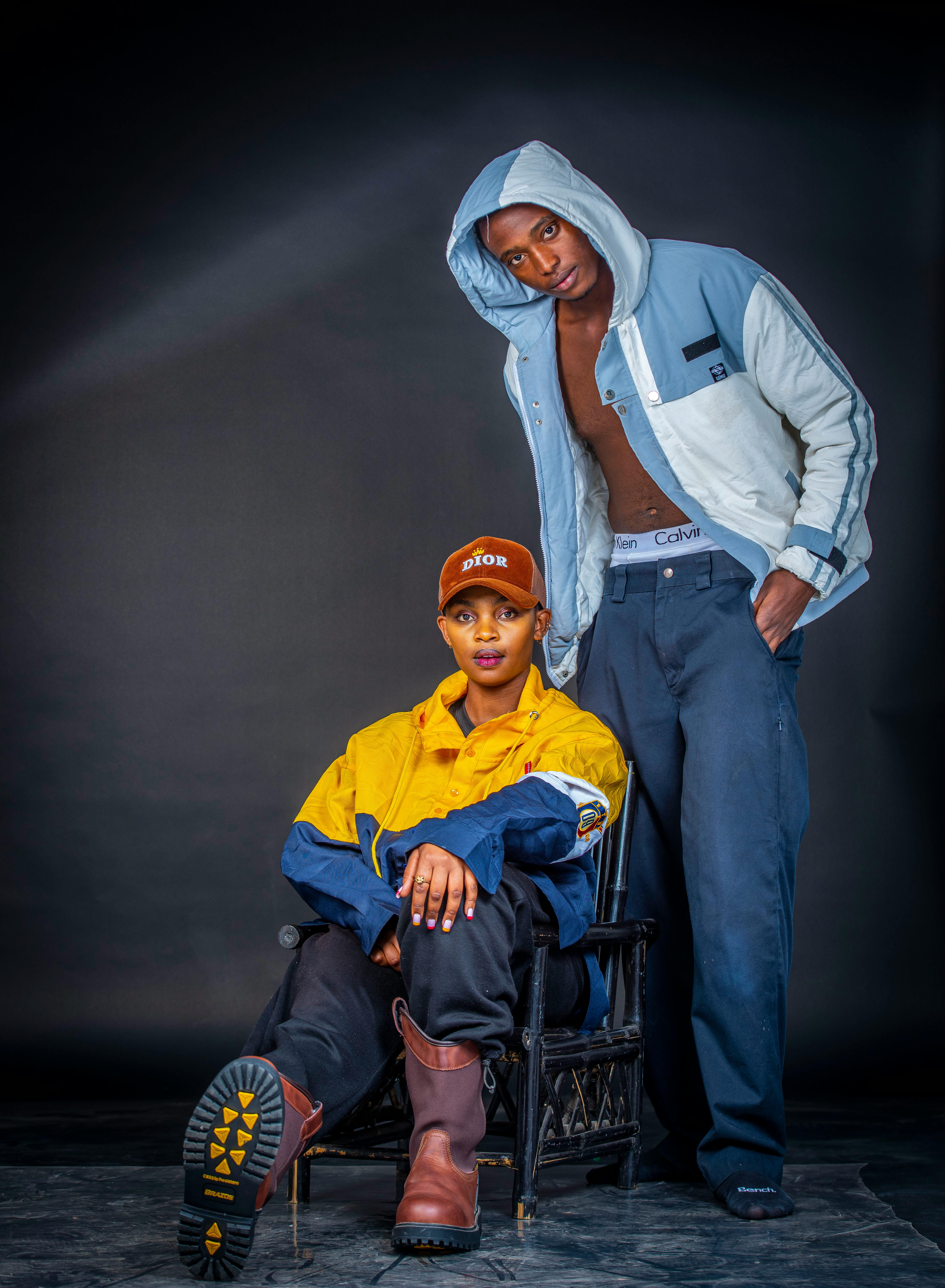 two men in jackets and pants sitting on a chair