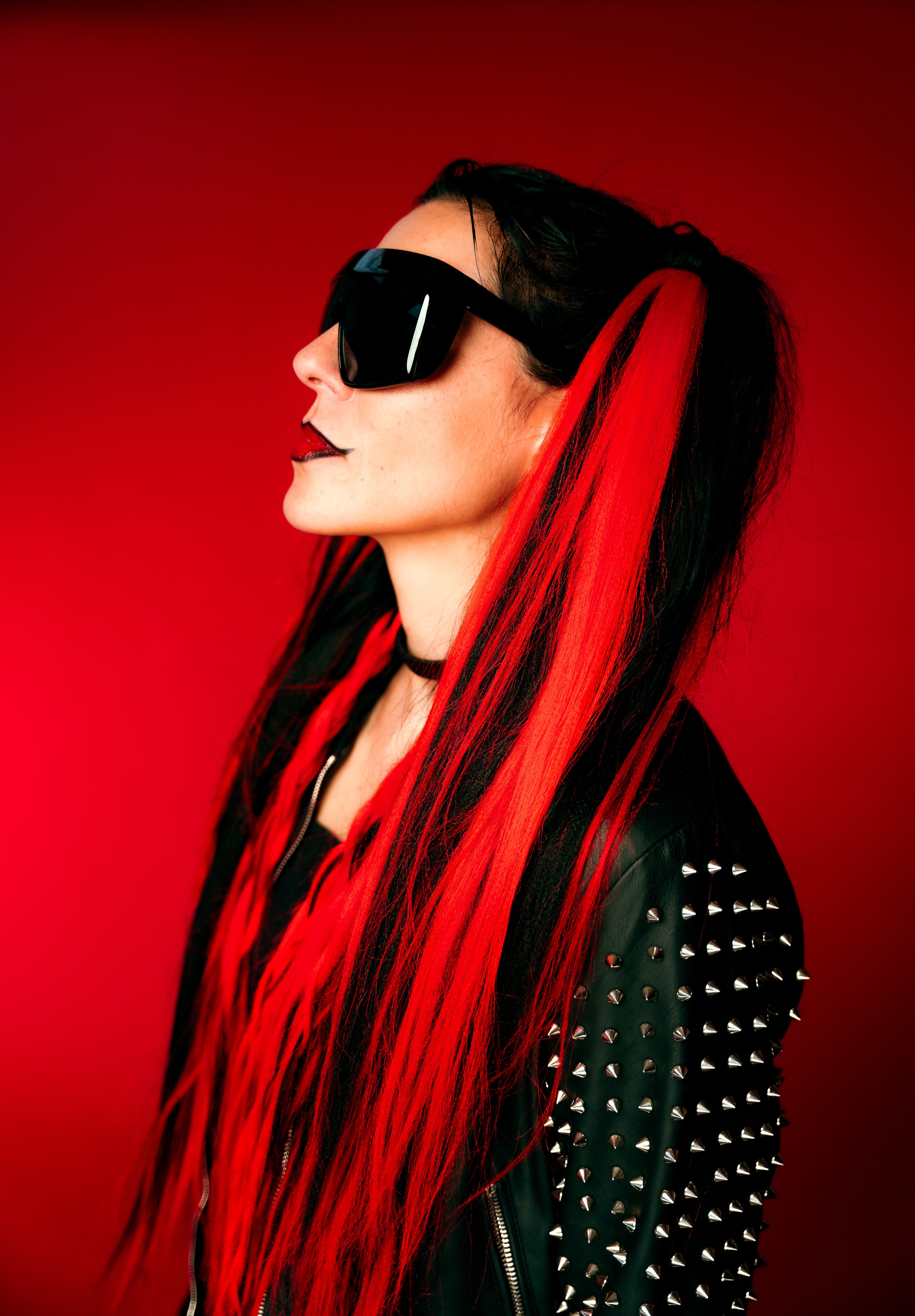 Portrait of a woman with sunglasses and red hair, in a black leather jacket with spikes.
