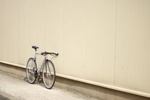 A lone bicycle leans against a minimalist beige wall in an urban setting, depicting simplicity.