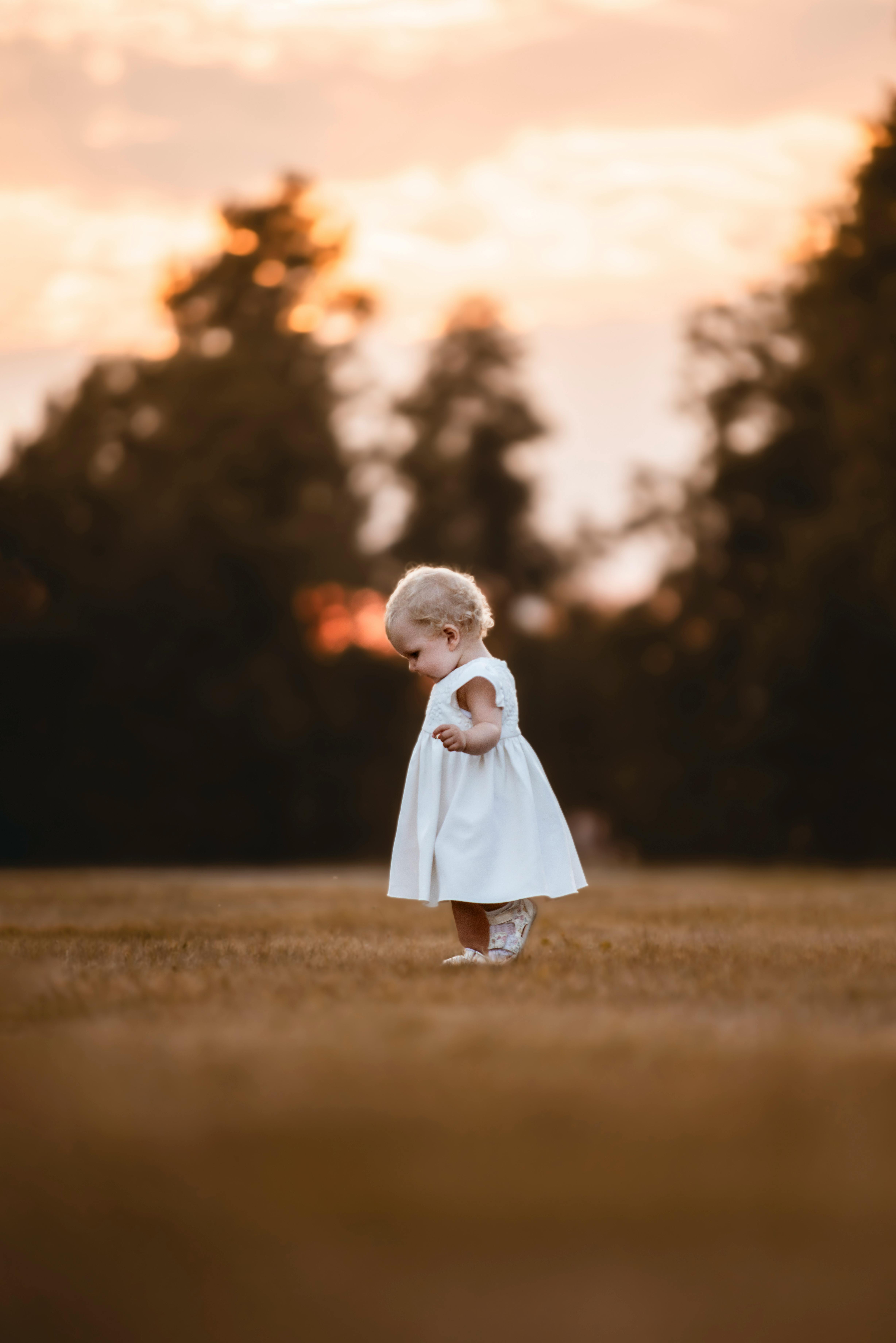 a baby girl in a white dress standing in a field