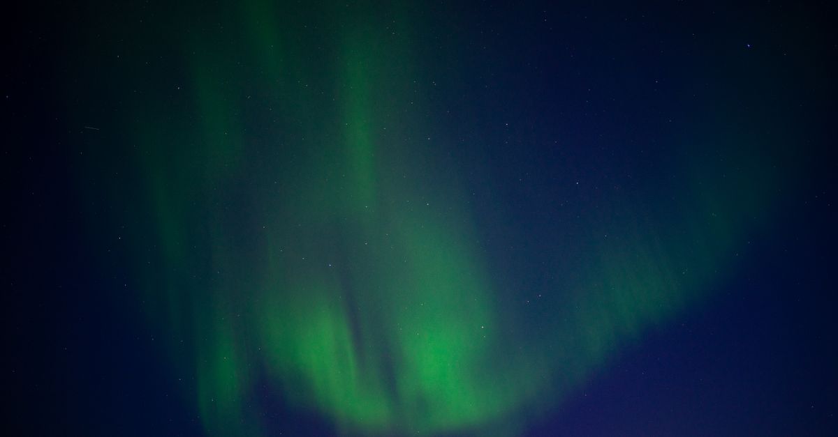 Green northern lights aurora dancing over snow-covered landscape in Arctic winter