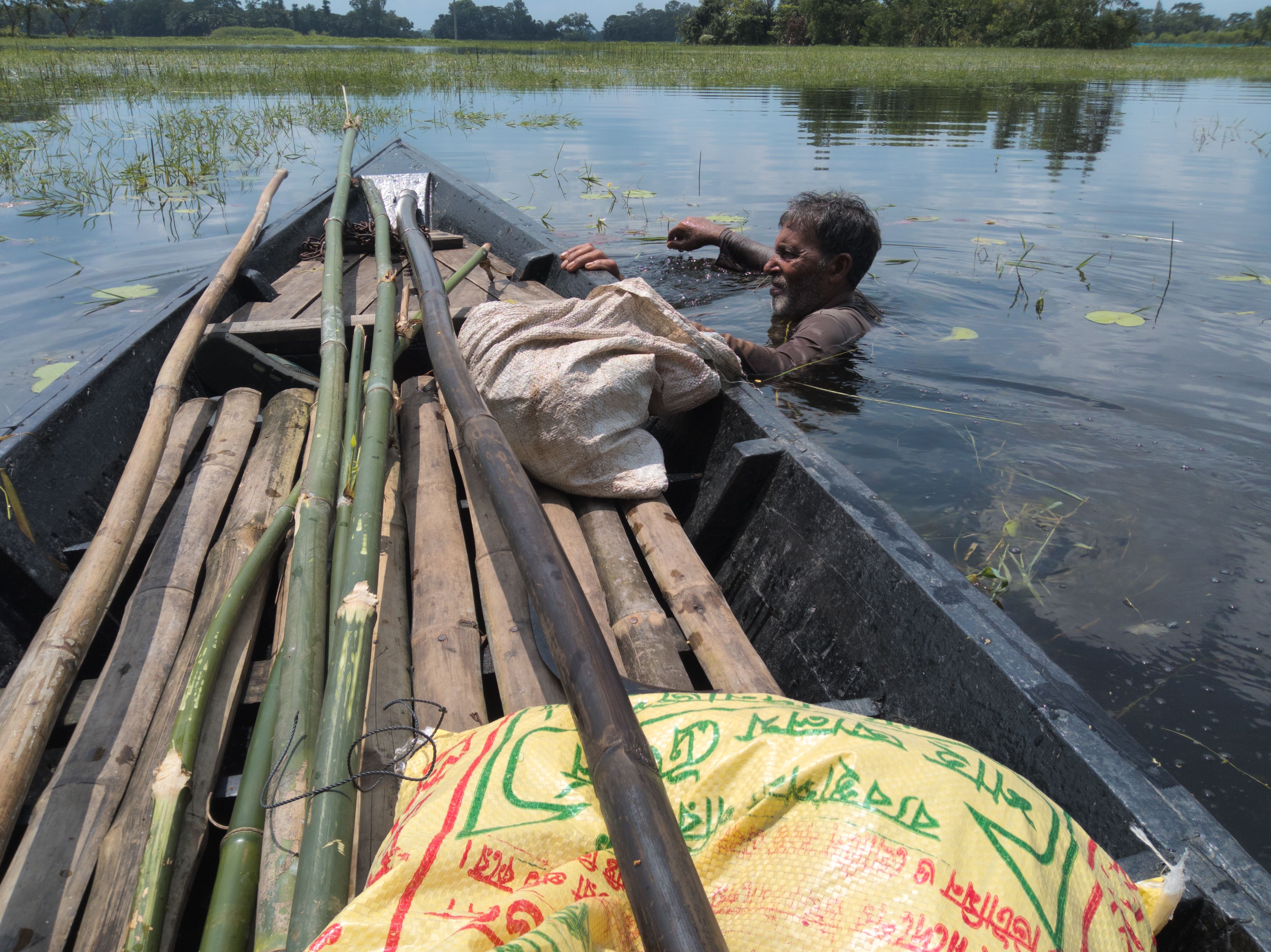 A fisherman navigates a shallow flooded area with his loaded boat, surrounded by nature.