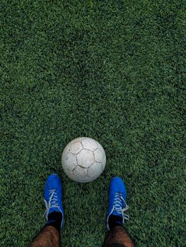 A soccer ball on synthetic turf with player's blue shoes visible, outdoor sports scene.