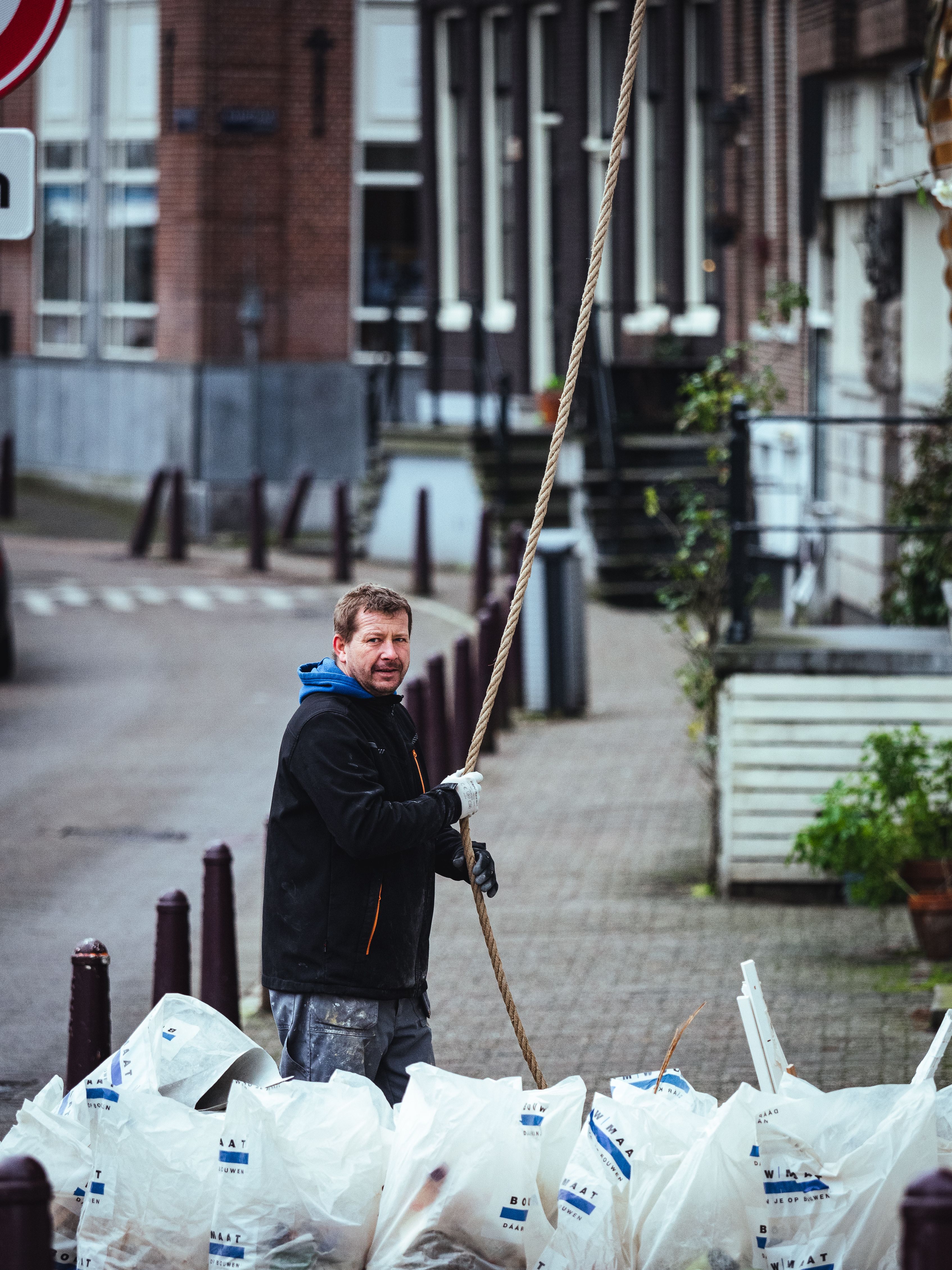 A man manages rope and garbage bags on a city street in daytime.