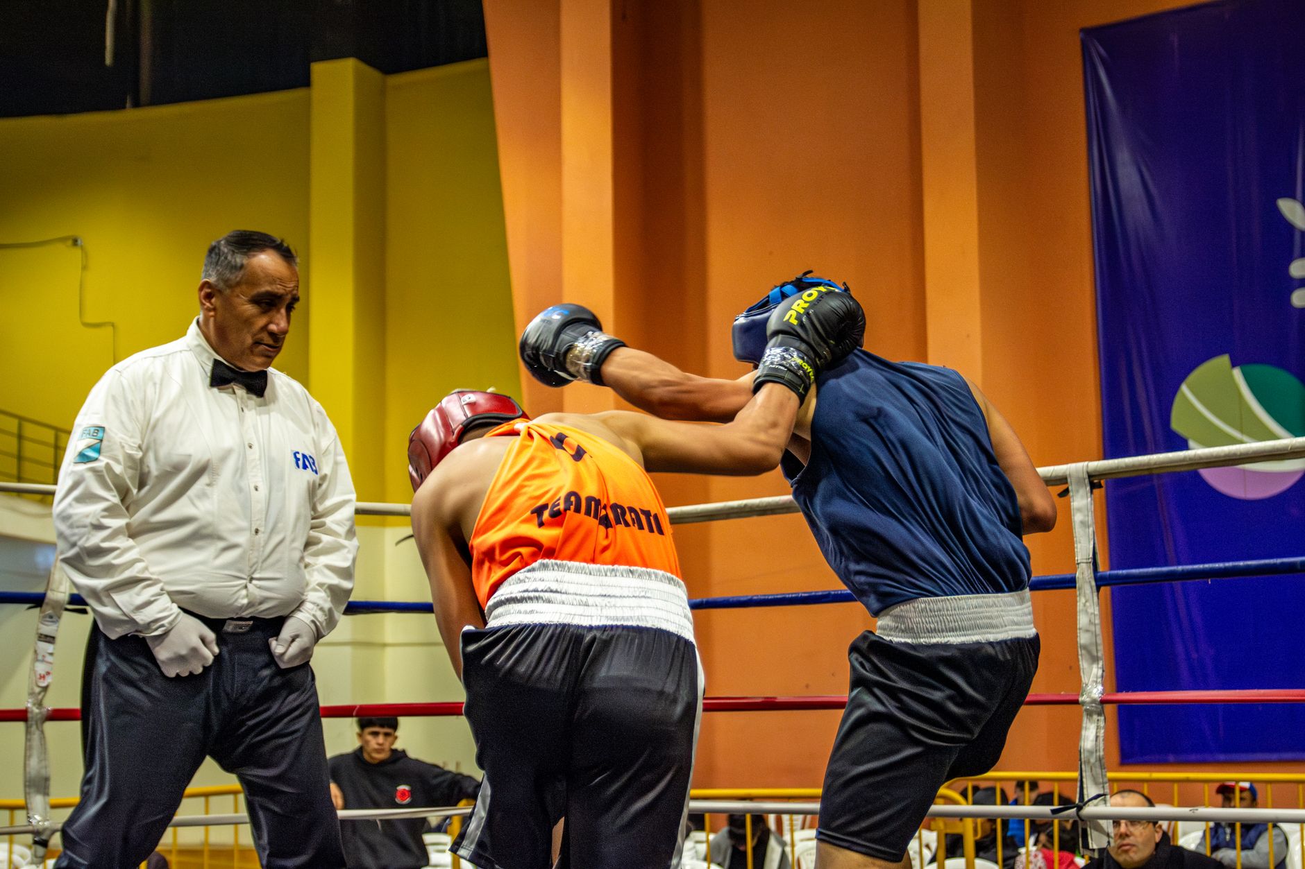 Boxing match action shot with two fighters and referee in a boxing ring.