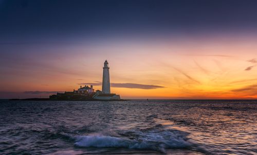 Free Serene sunset view of a lighthouse near the ocean with gentle waves. Stock Photo