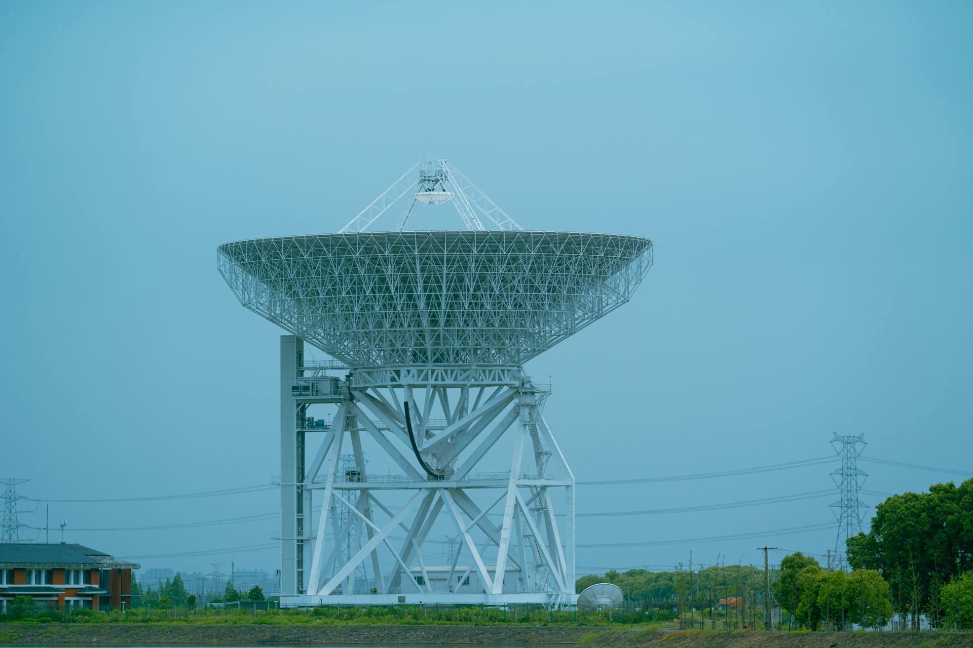 A large white satellite dish standing outdoors in a rural area, used for communication.