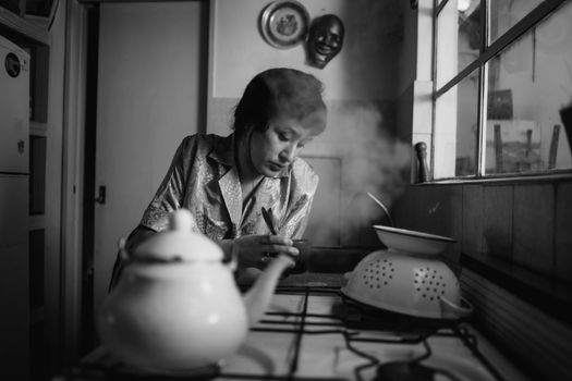 A monochrome scene of a woman in a retro kitchen with steaming kettle.