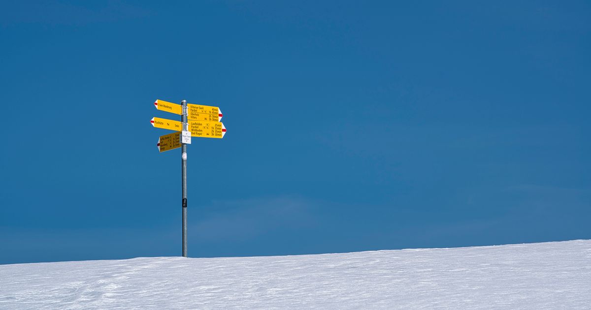 Bright yellow signpost standing in a snowy winter landscape under a clear blue sky