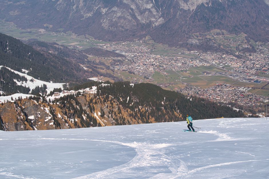 A skier enjoying fresh snow on a scenic alpine slope with a town view.