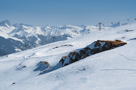 Panoramic view of a snowy alpine ski resort with mountain peaks and ski slopes under a clear blue sky.
