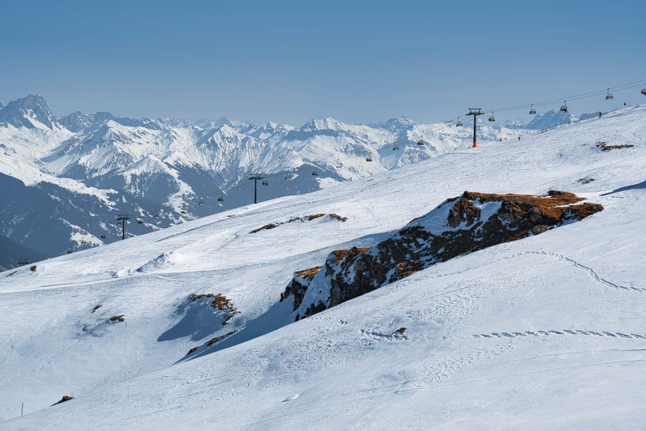 Panoramic view of a snowy alpine ski resort with mountain peaks and ski slopes under a clear blue sky.