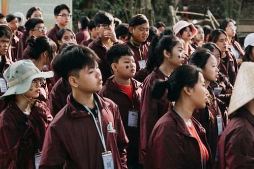 Free A large group of teenagers wearing badges and jackets at an outdoor event, attentive and engaged. Stock Photo