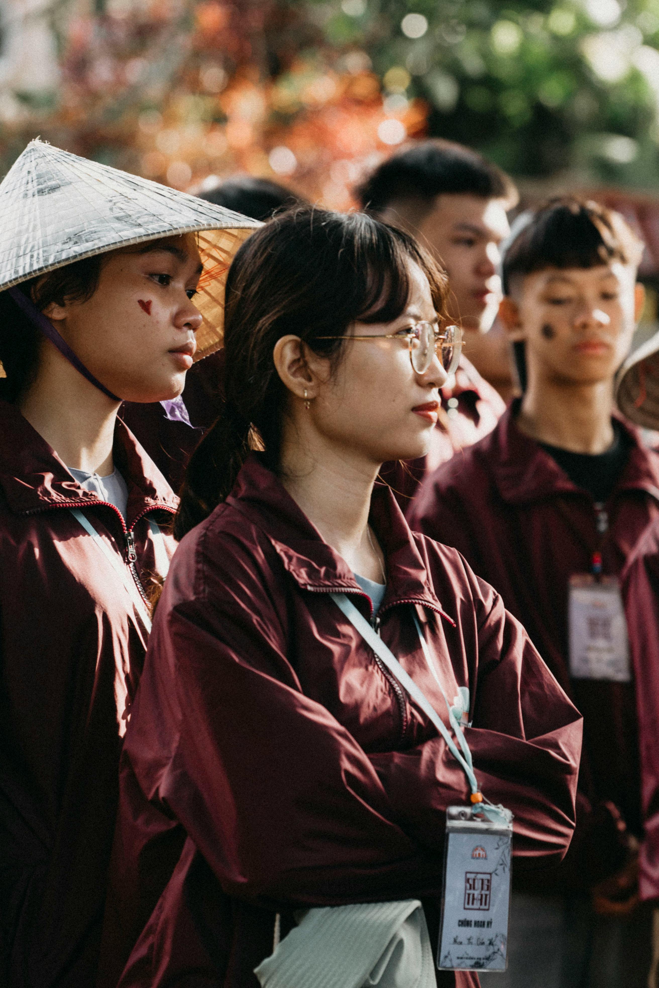 Group of young adults wearing maroon jackets and tags standing outdoors, engaging in an event.