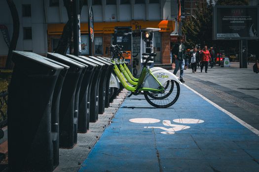 Colorful bicycle rental station on a busy urban street with people walking and vehicles passing.