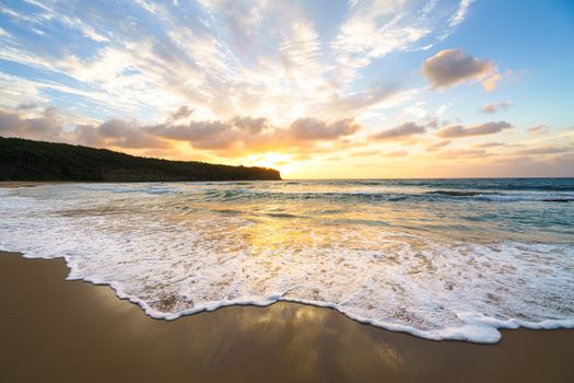 A serene sunset over a sandy beach with gentle waves and vibrant colors.