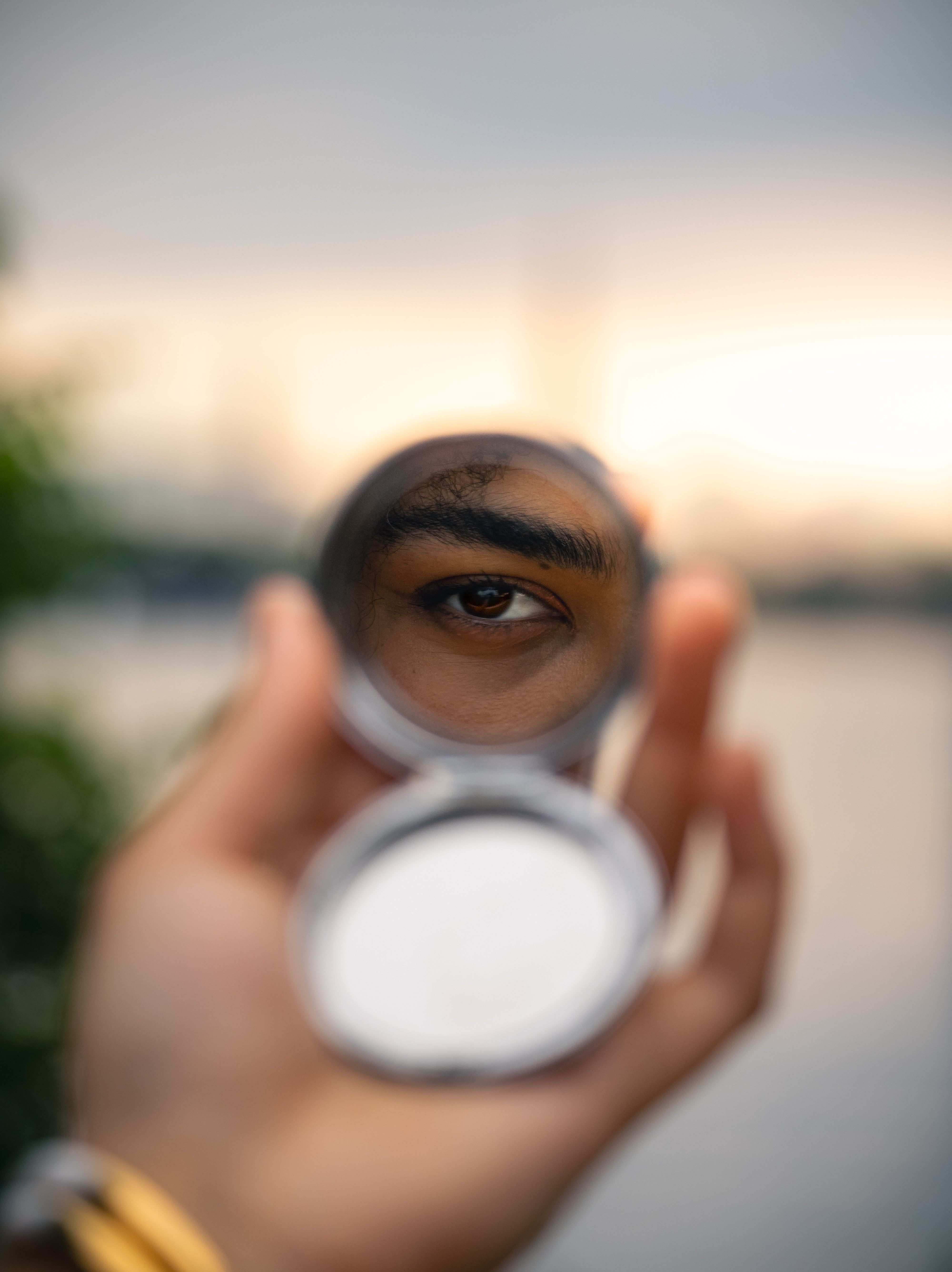Close-up of an eye reflected in a mirror held by a hand at sunset in Hamburg.