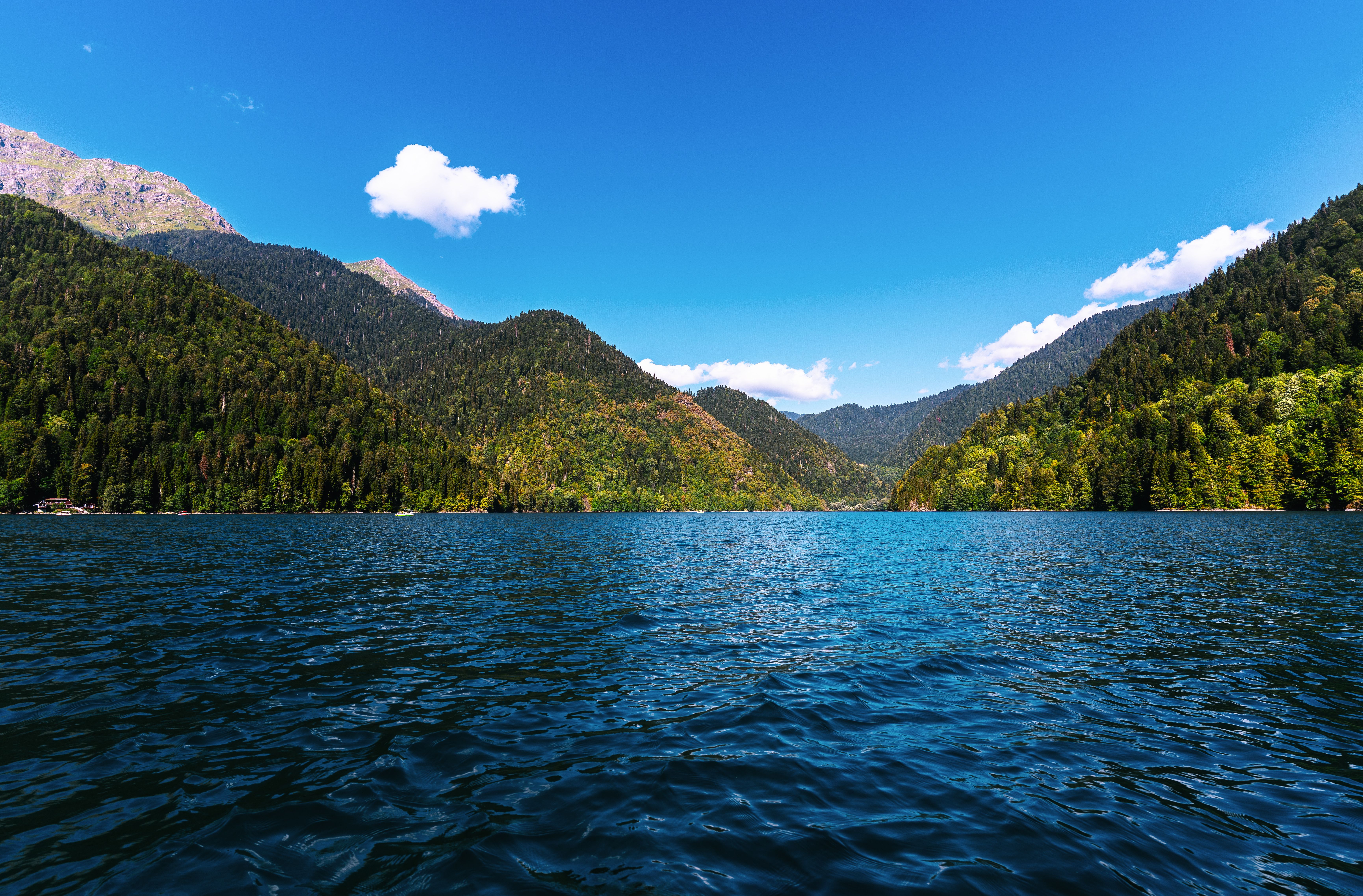 Scenic view of a tranquil mountain lake surrounded by lush forested hills under a clear blue sky.