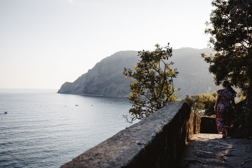 Free A serene view of the Ligurian coast with a person walking along a stone pathway at sunset. Stock Photo