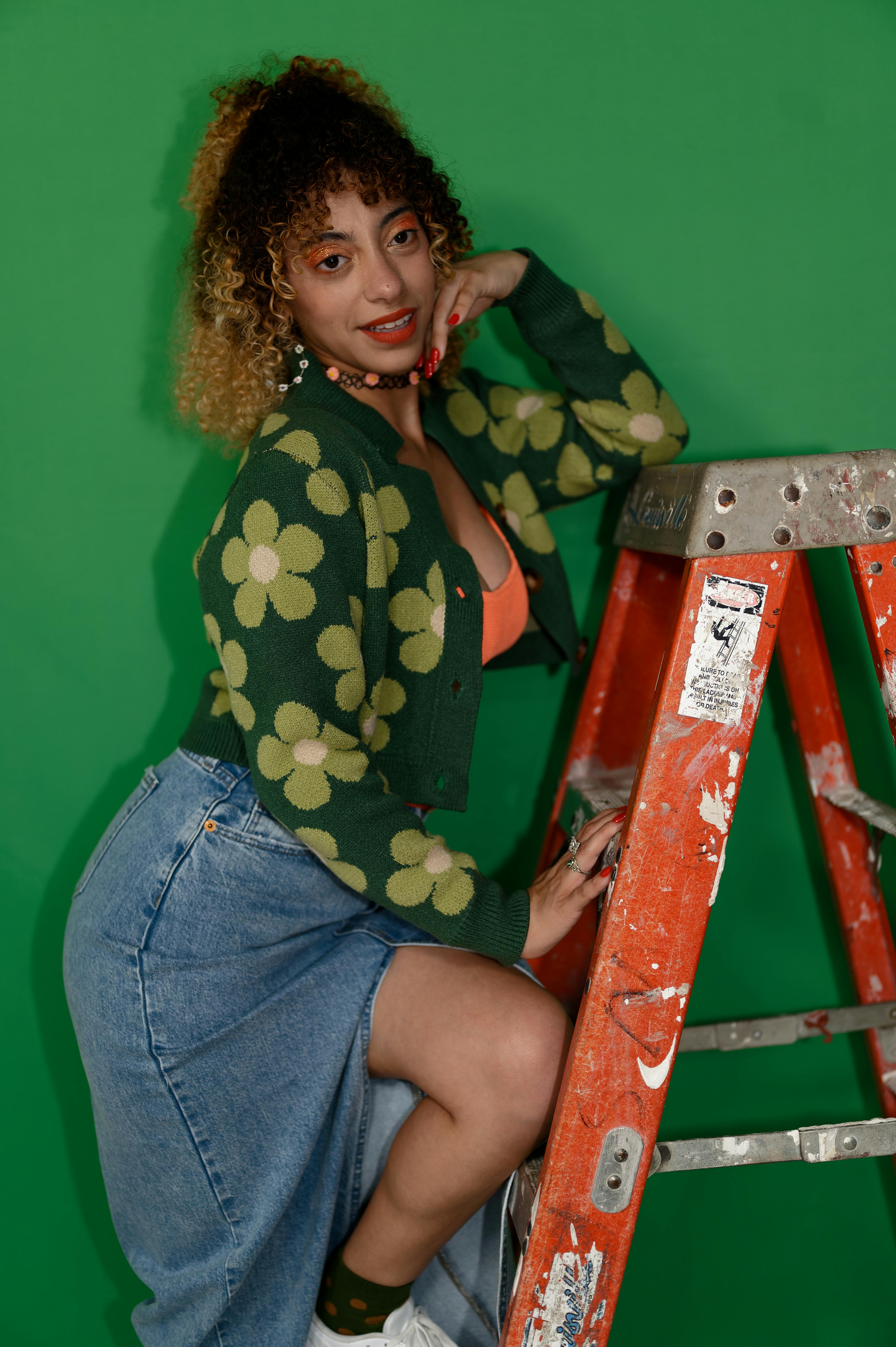 a woman sitting on a ladder with a green screen background