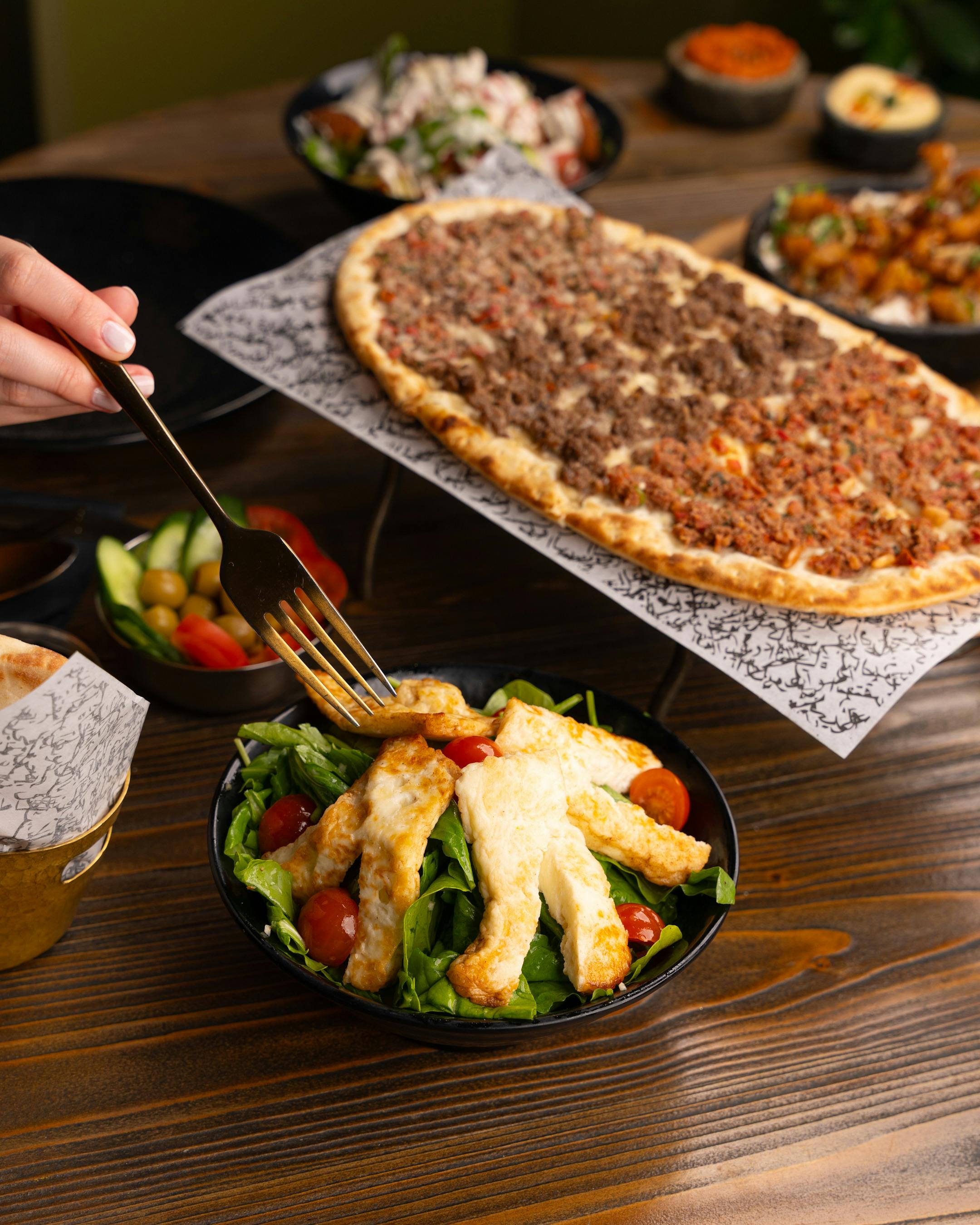 a person holding a fork over a pizza and salad