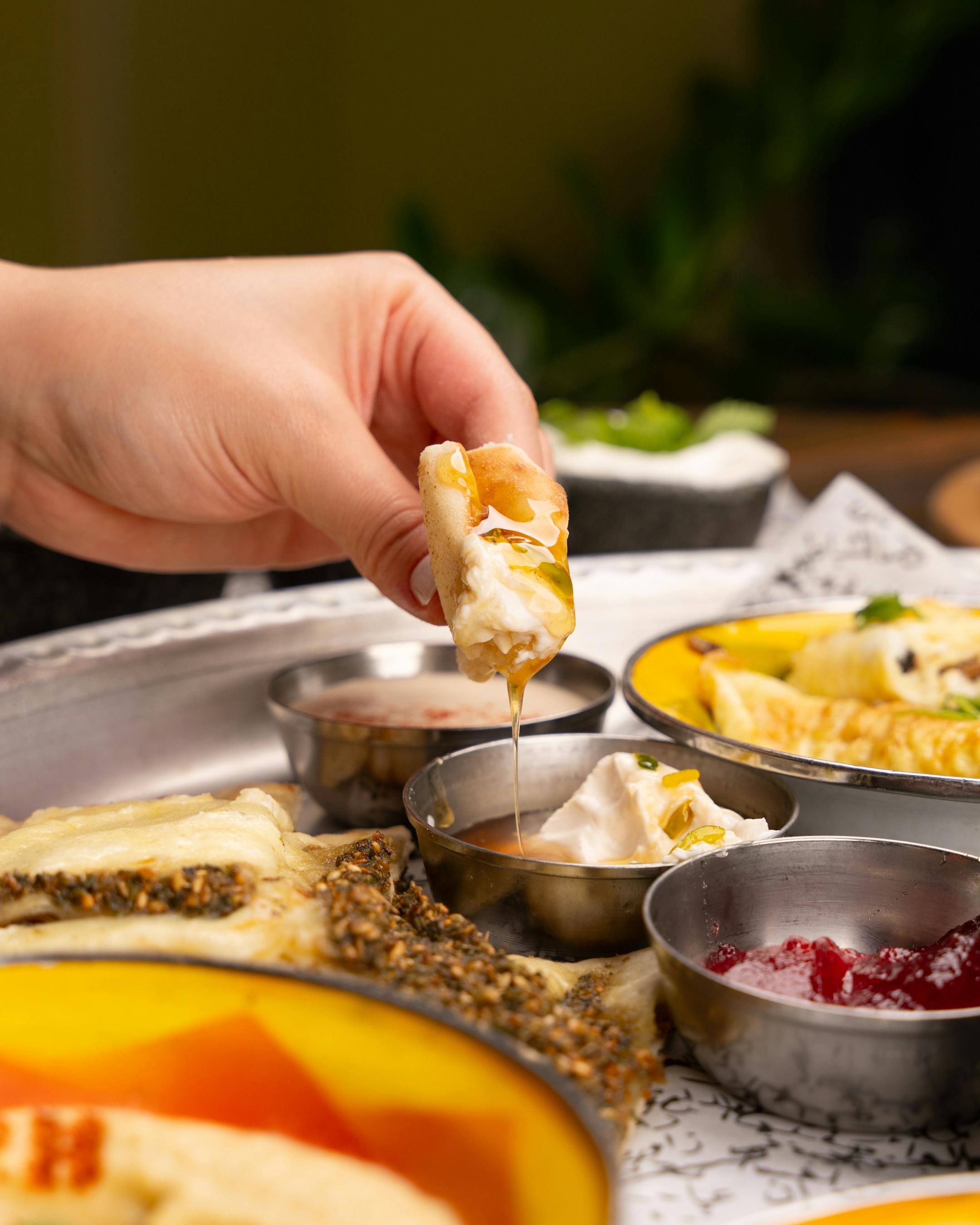 Close-up of a hand dipping bread in various Middle Eastern sauces. Vibrant and appetizing.