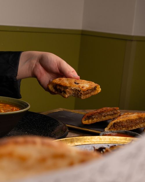 Free A hand holding a grilled sandwich, ready to eat, with soup in the background. Stock Photo