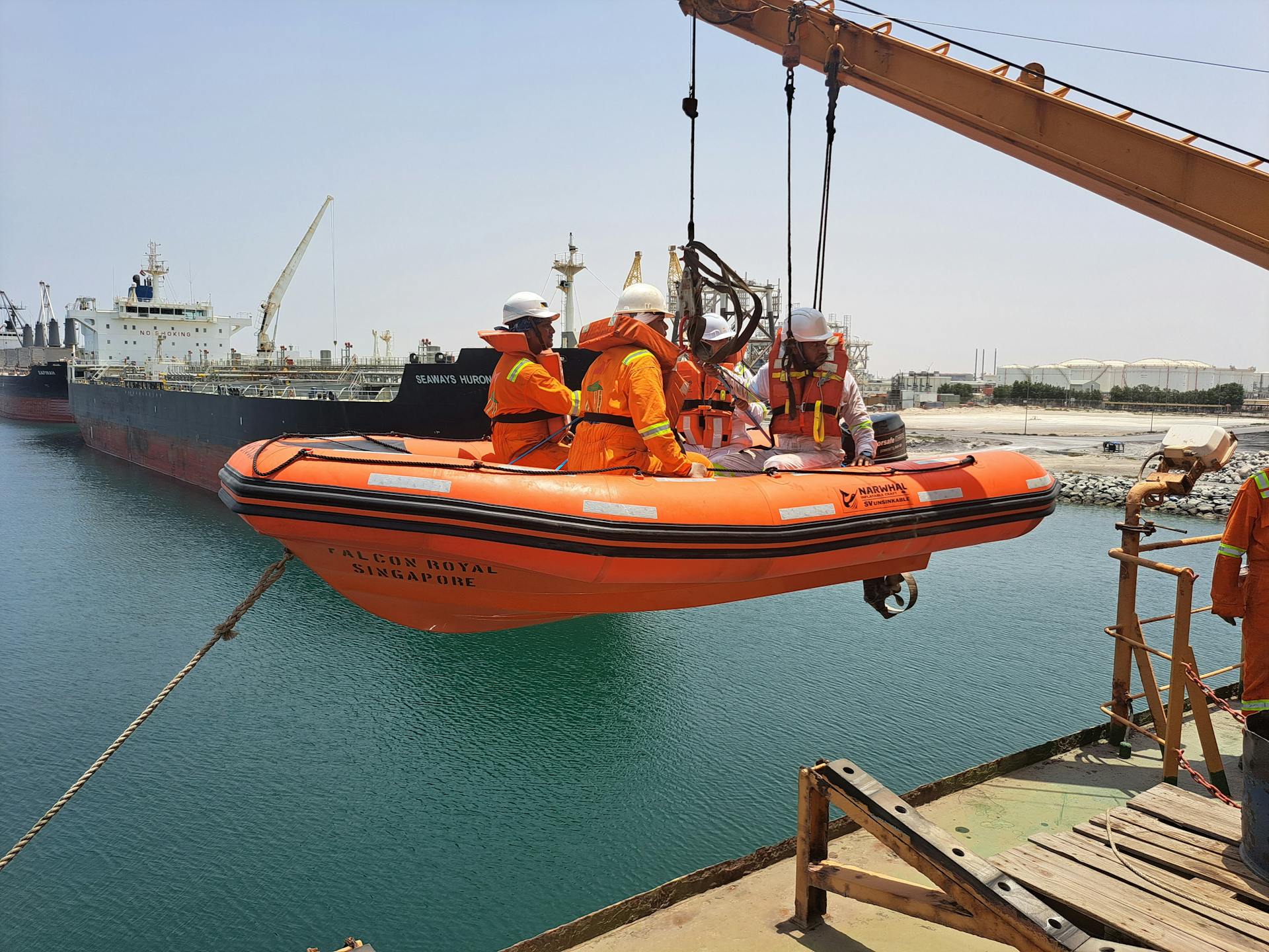Workers operate a lifeboat during a safety drill in a bustling port setting.
