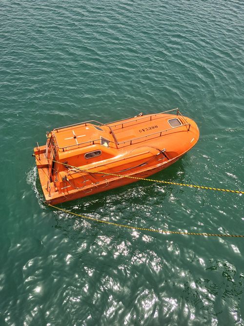 Free Orange lifeboat floating on calm sea with clear blue water under sunlight. Stock Photo