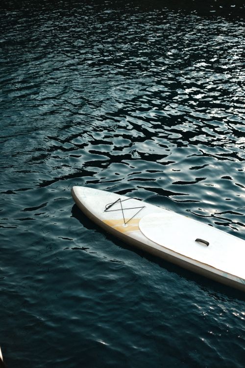 Free A serene paddleboard floating on glistening deep blue water, capturing a summer leisure vibe. Stock Photo