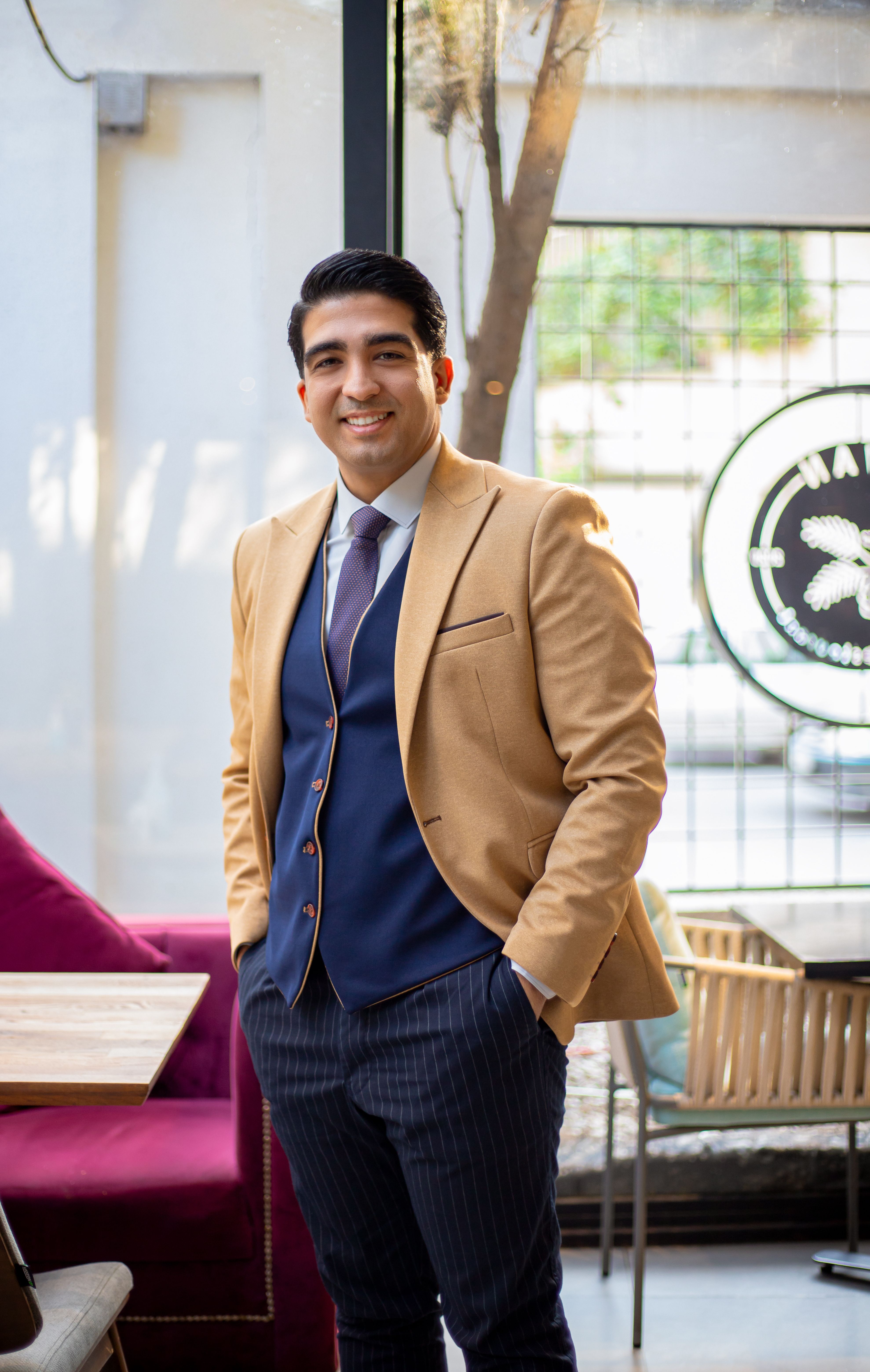 Confident young man in a stylish suit standing indoors with a warm smile.