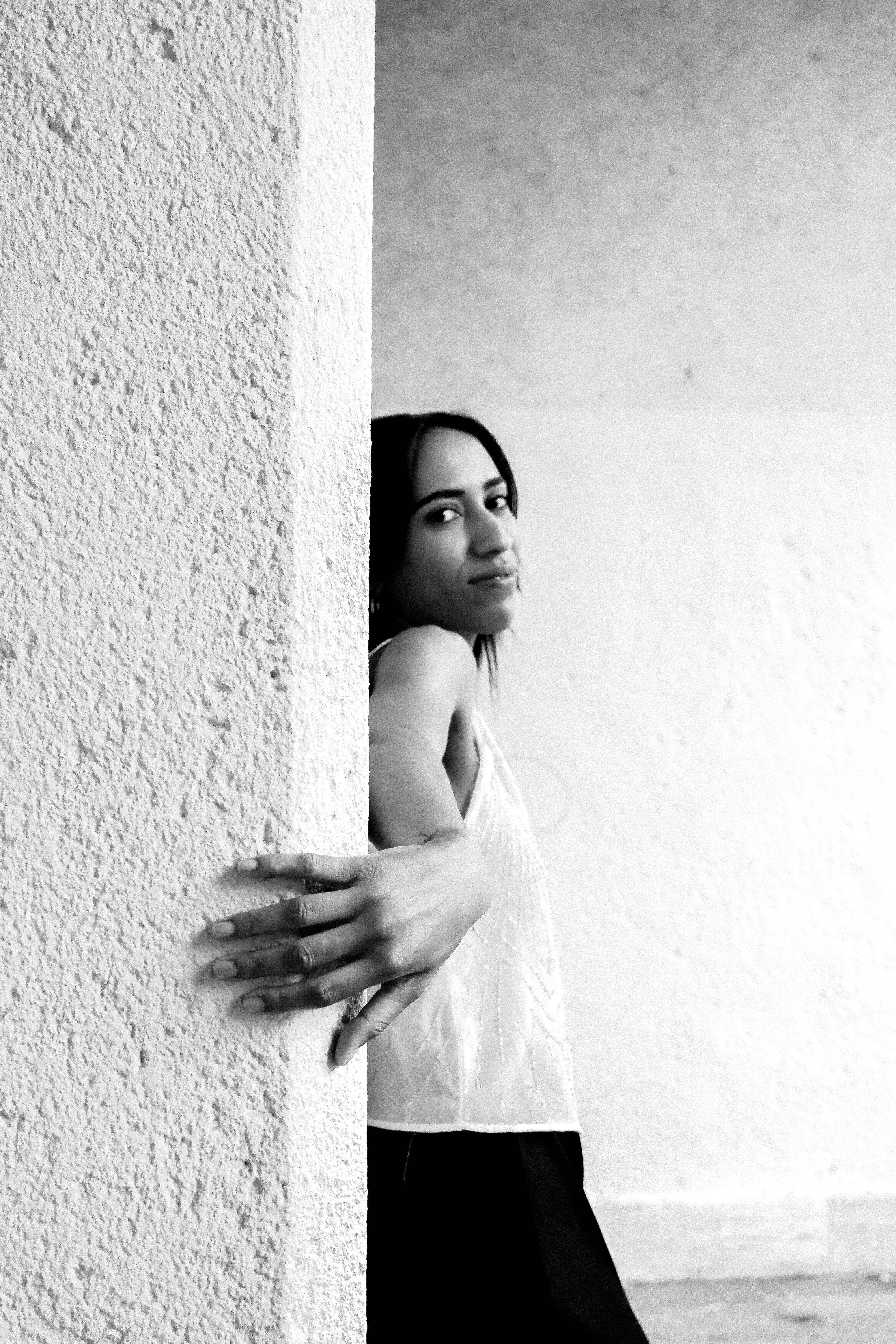 Black and white portrait of a young woman leaning against a textured wall.