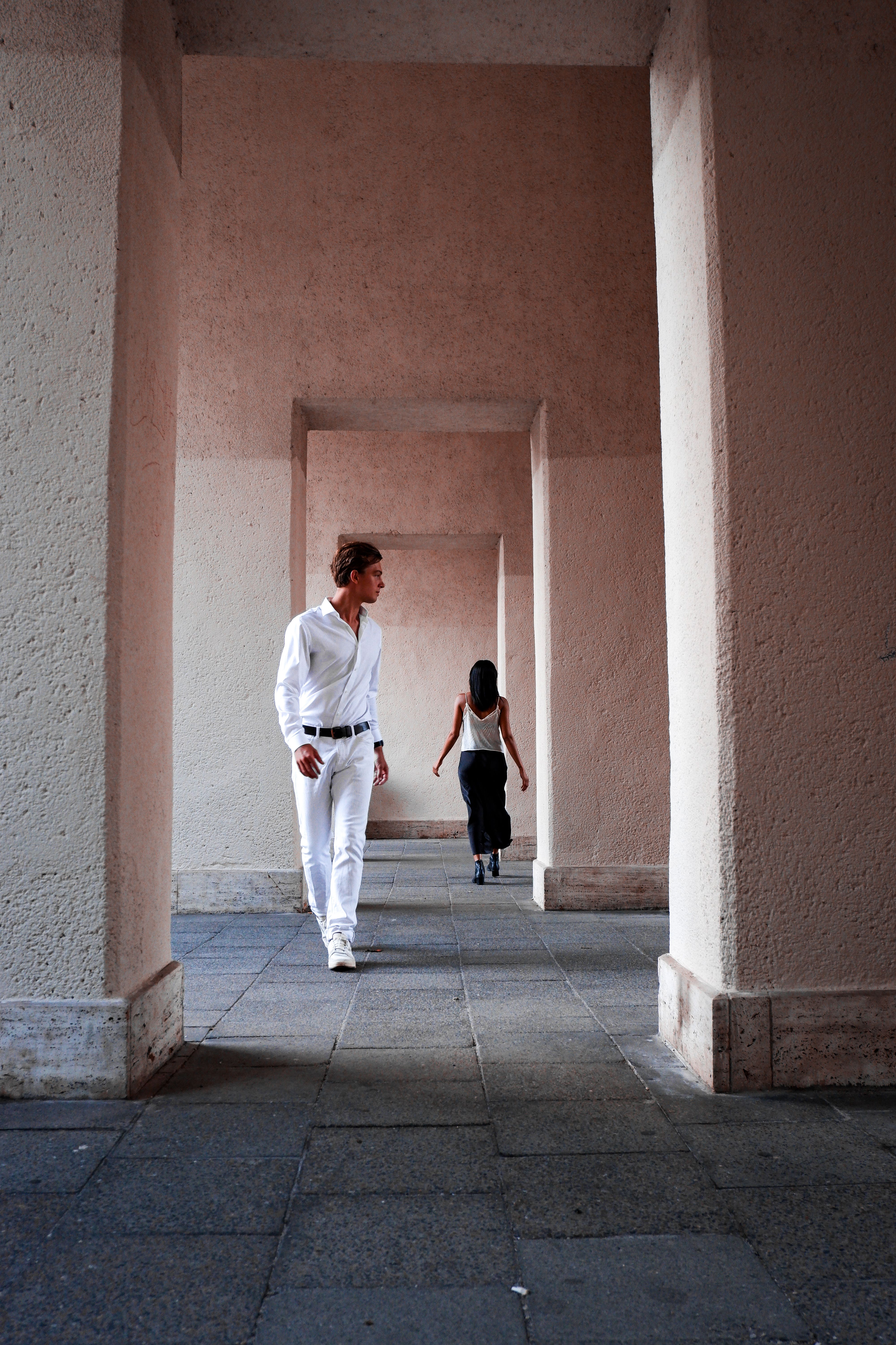 Stylish man and woman walking through a modern corridor with concrete pillars.