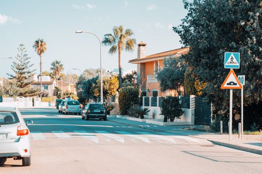 Sunny suburban street with palm trees and cars in Palma de Mallorca, Spain, showcasing Mediterranean architecture.