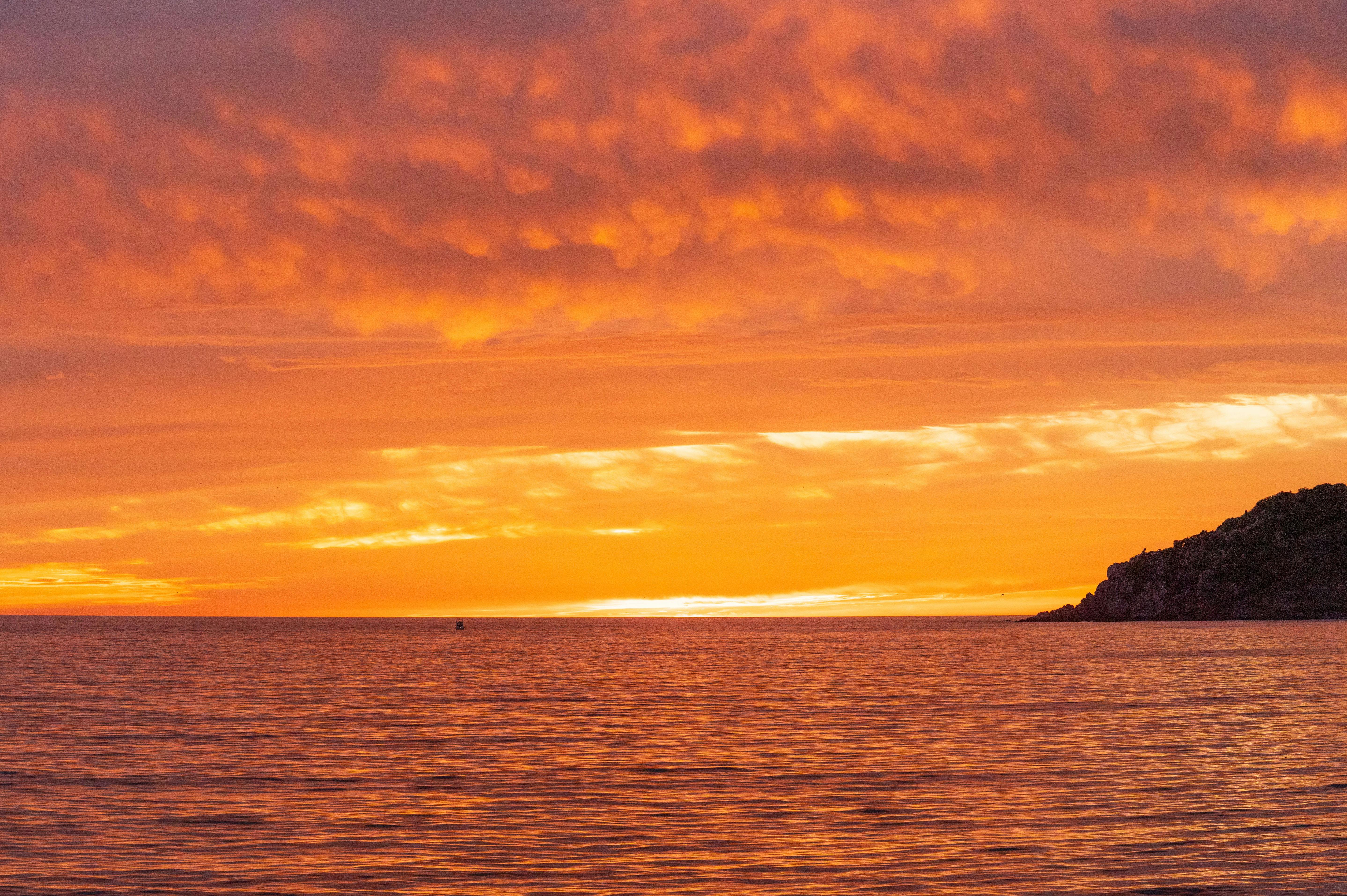 a sunset over the ocean with clouds and boats