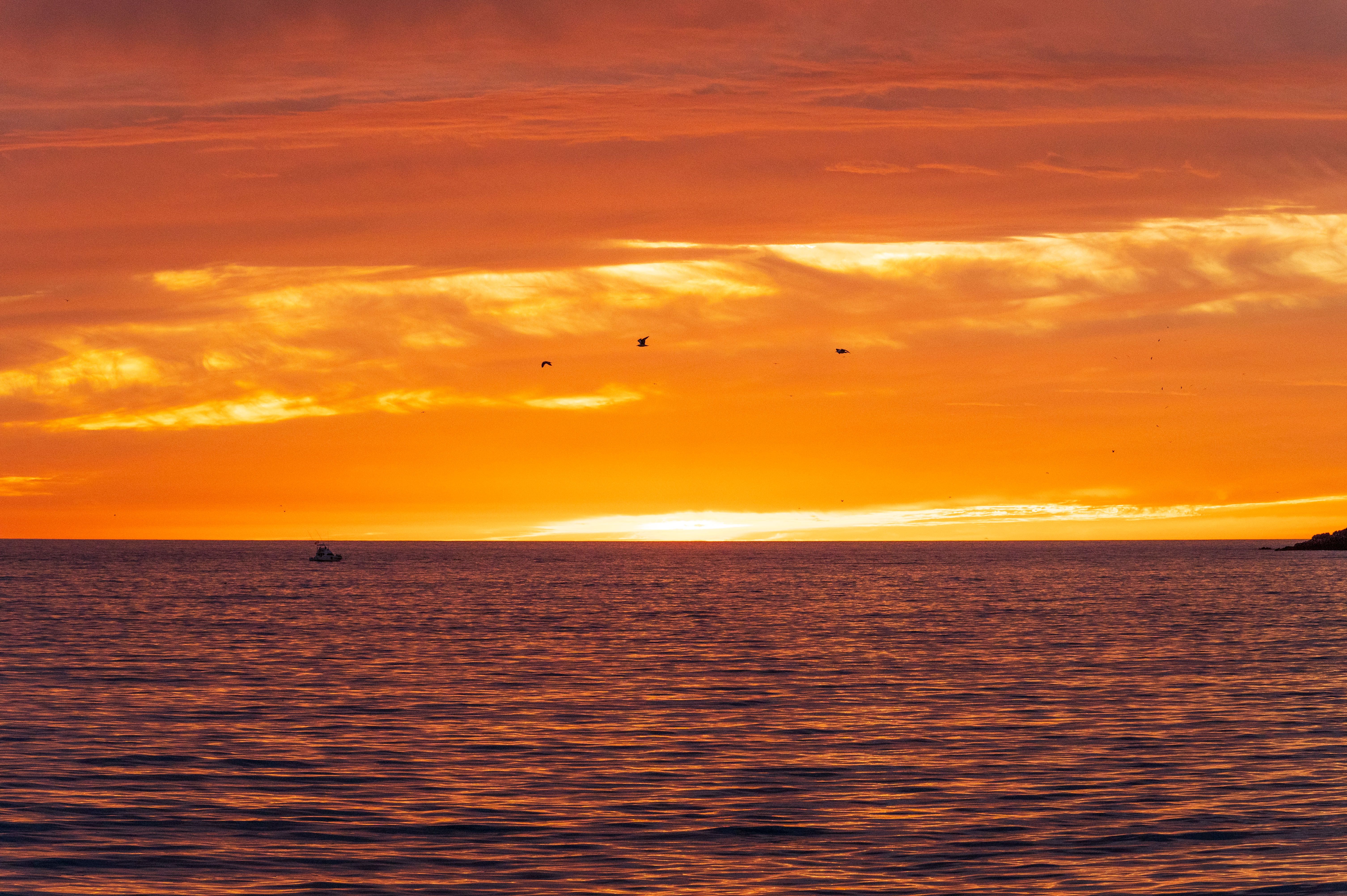 A sunset over the ocean with a boat in the distance · Free Stock Photo