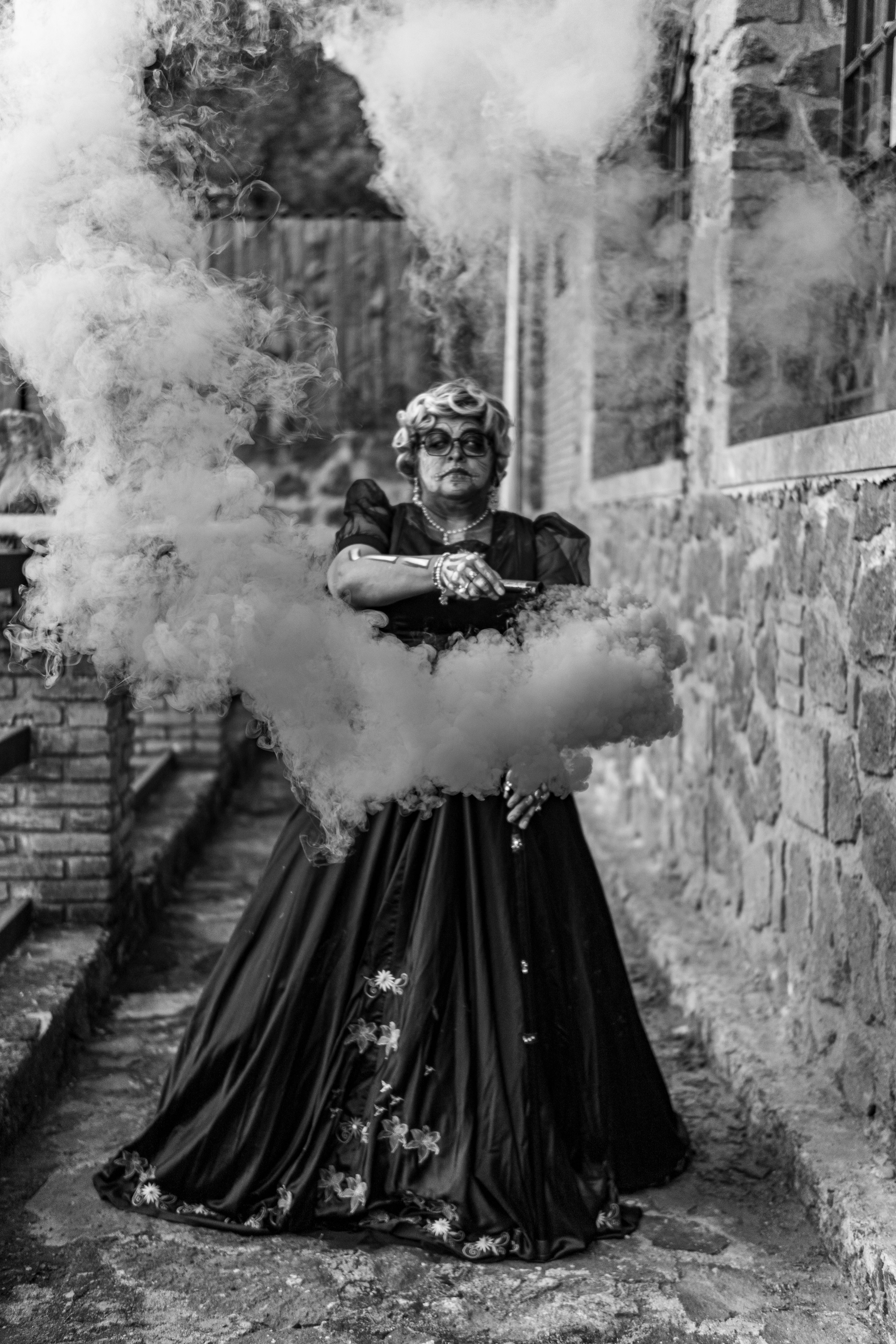 A woman in Catrina makeup and dress creates a dramatic scene with smoke, celebrating Dia de los Muertos.