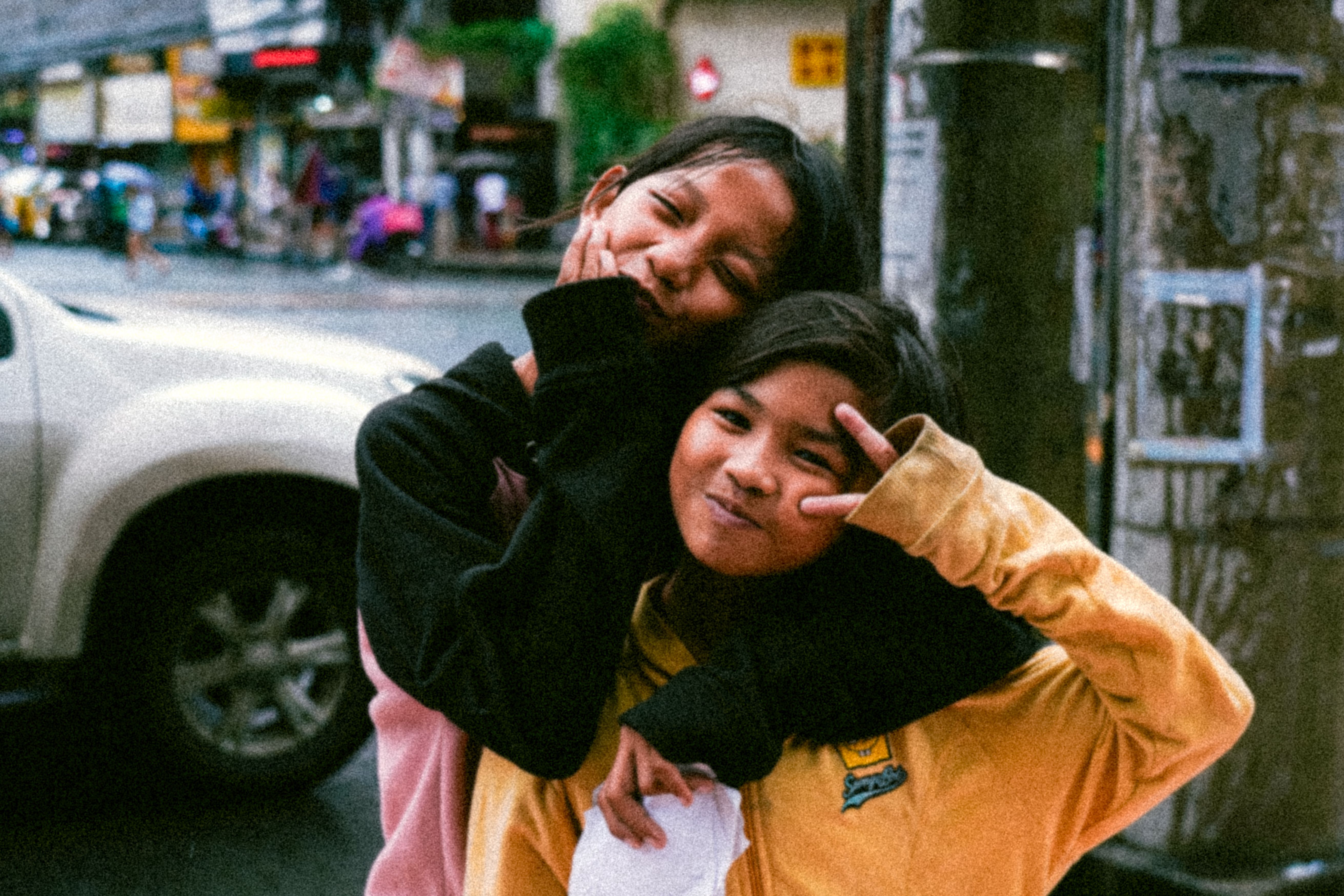 Two smiling friends pose playfully together on a vibrant urban street.