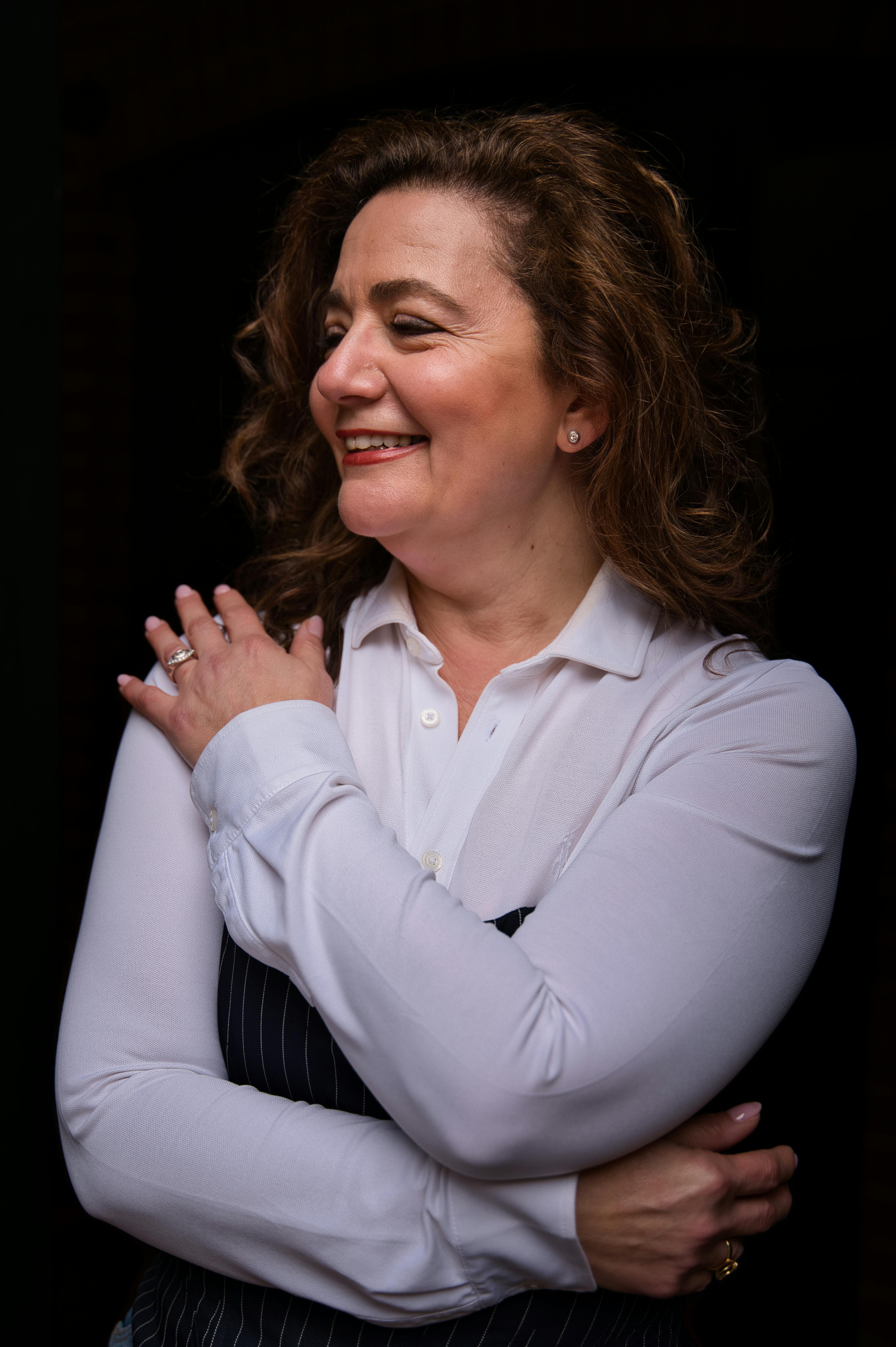 Portrait of a joyful woman in formal attire, smiling warmly indoors.