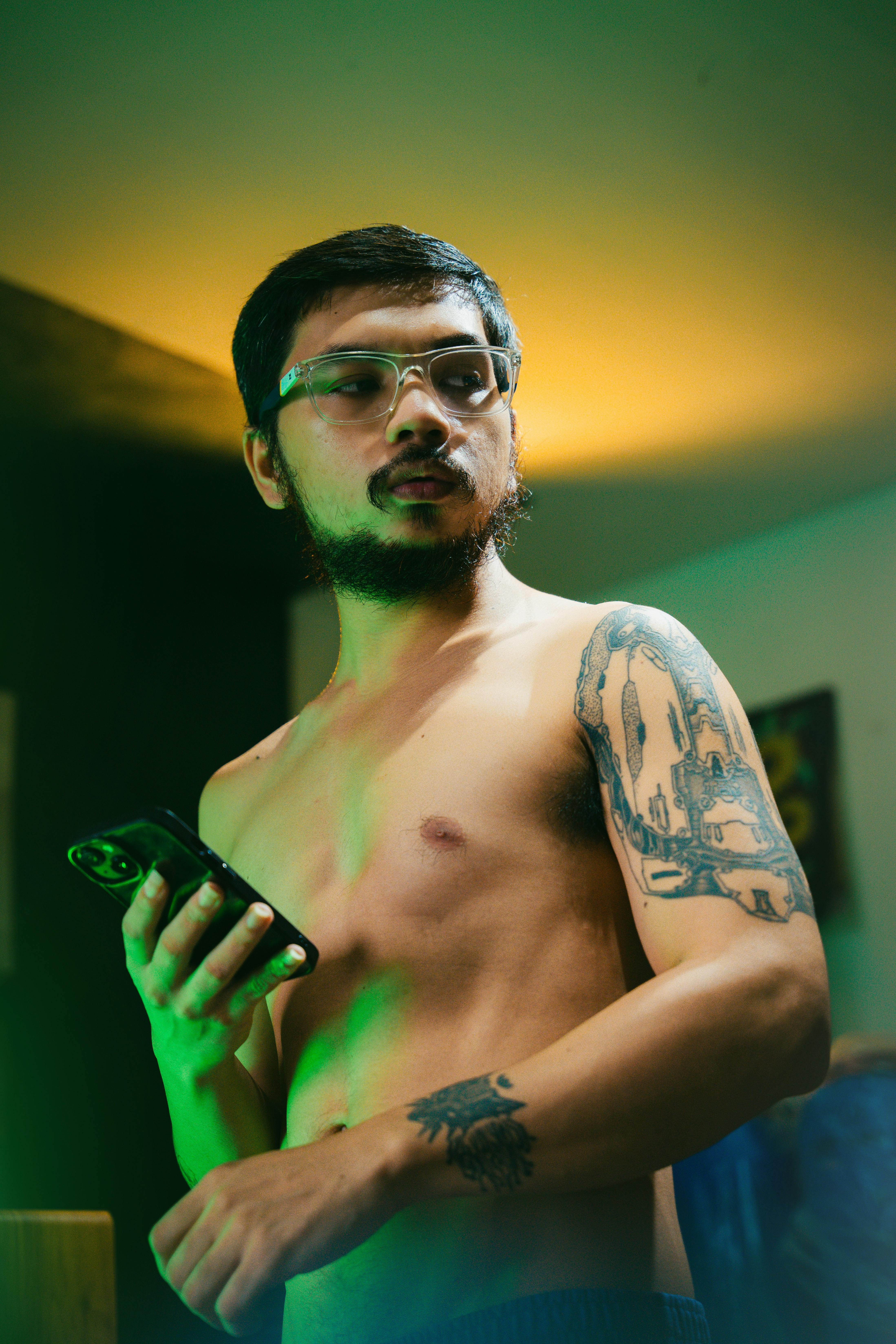 a shirtless man with tattoos holding a cell phone