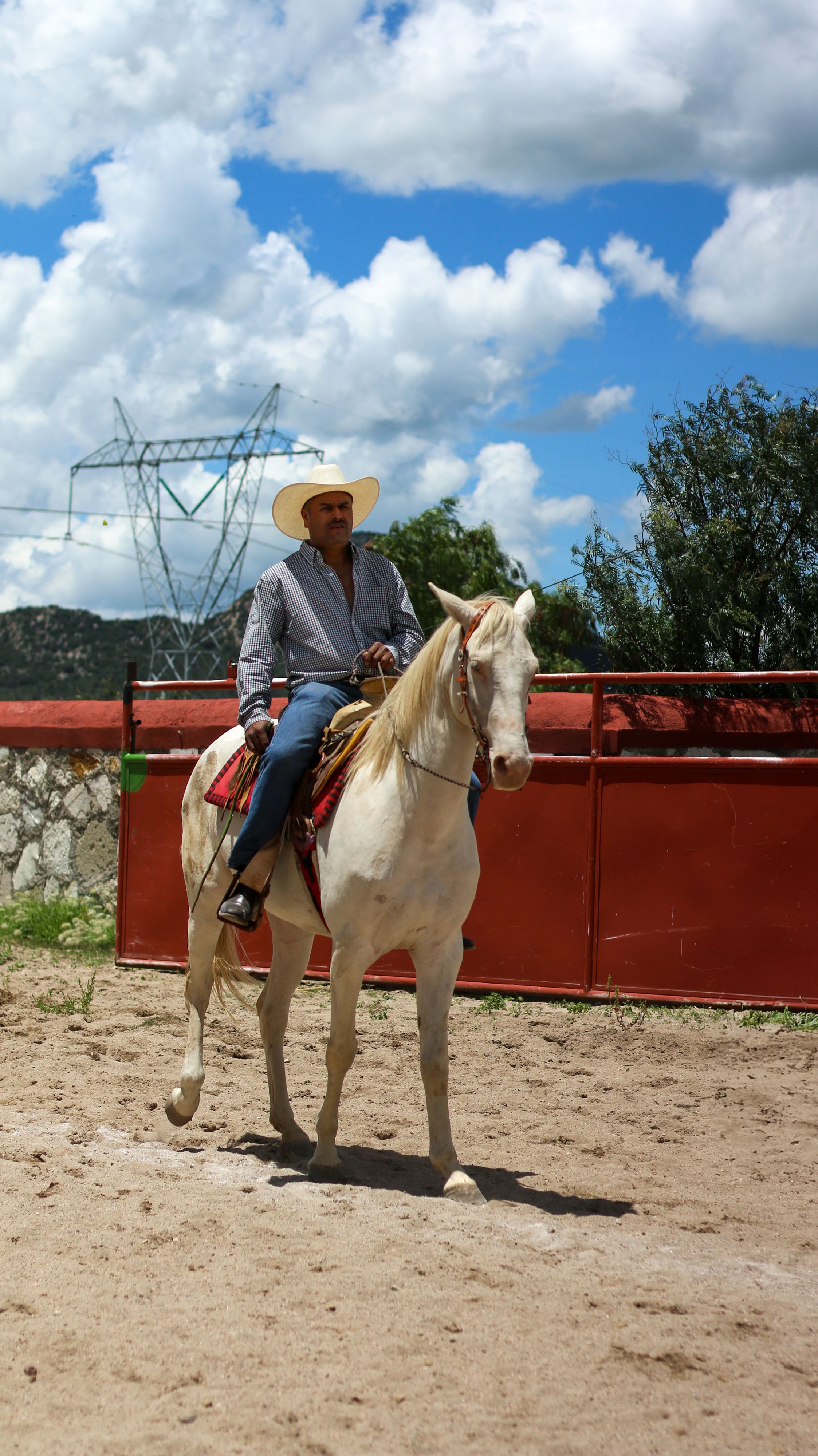 A horseman in traditional attire rides a horse in San Juan Tizahuapan, Mexico under a bright sky.
