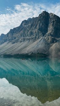 A tranquil scene of a mountain reflecting on a clear, turquoise lake under a blue sky.