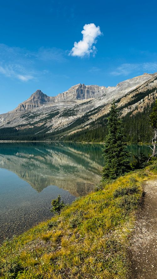 Free Explore tranquil mountain landscapes with a clear lake reflection and scenic hiking trail. Stock Photo