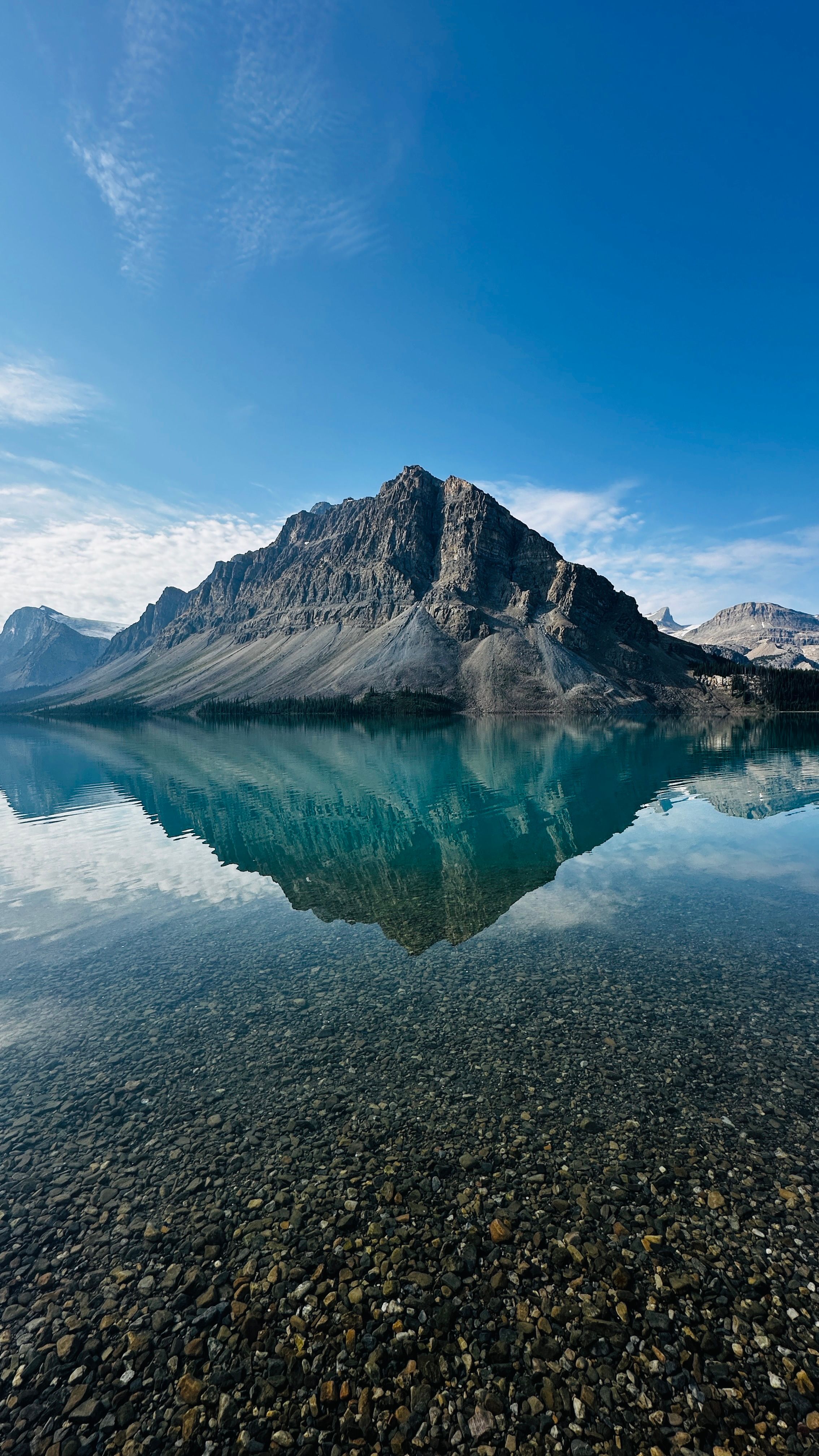 A breathtaking mountain view reflected in a clear, tranquil lake under a bright blue sky.