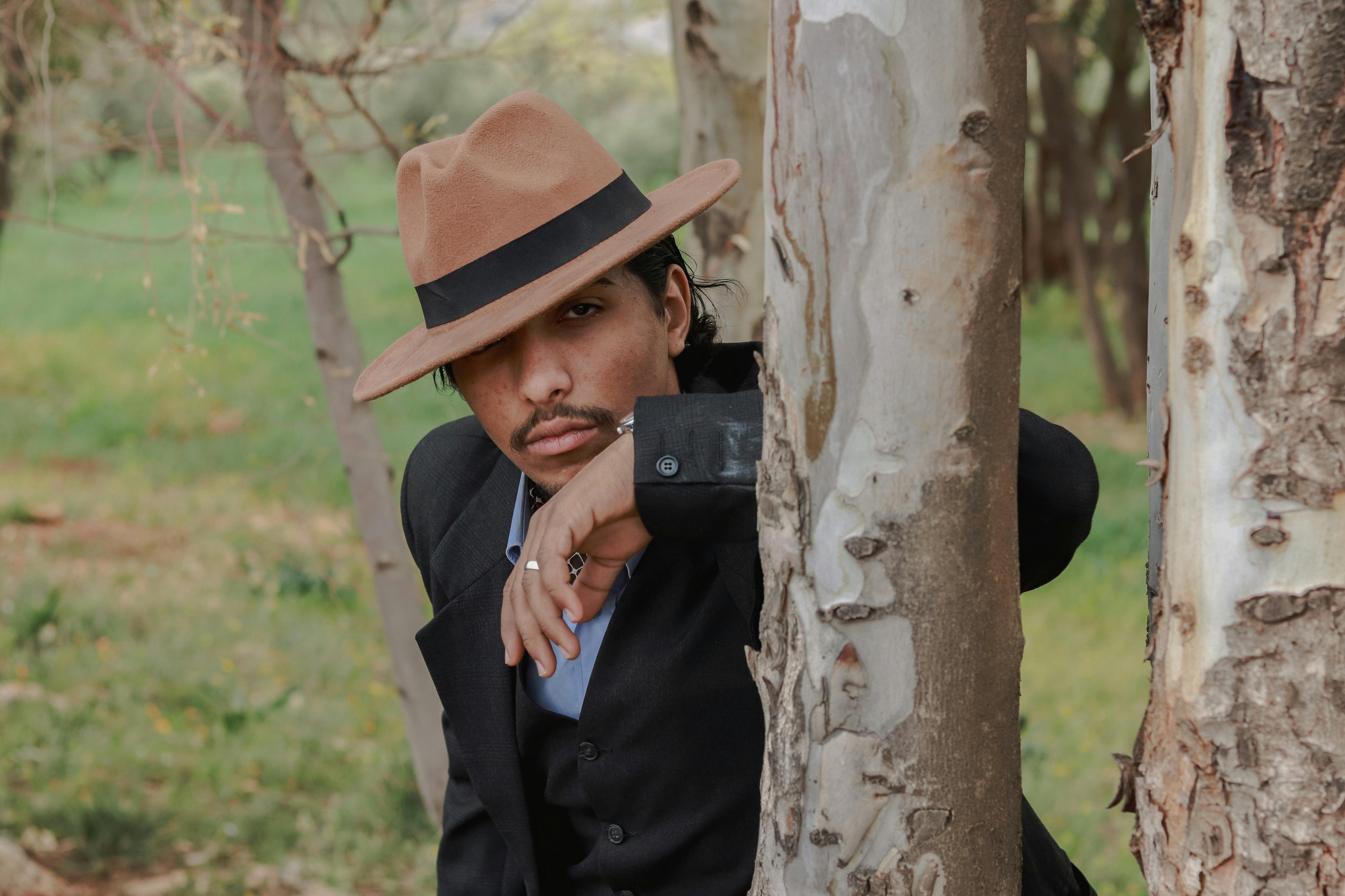 a man in a hat leaning against a tree