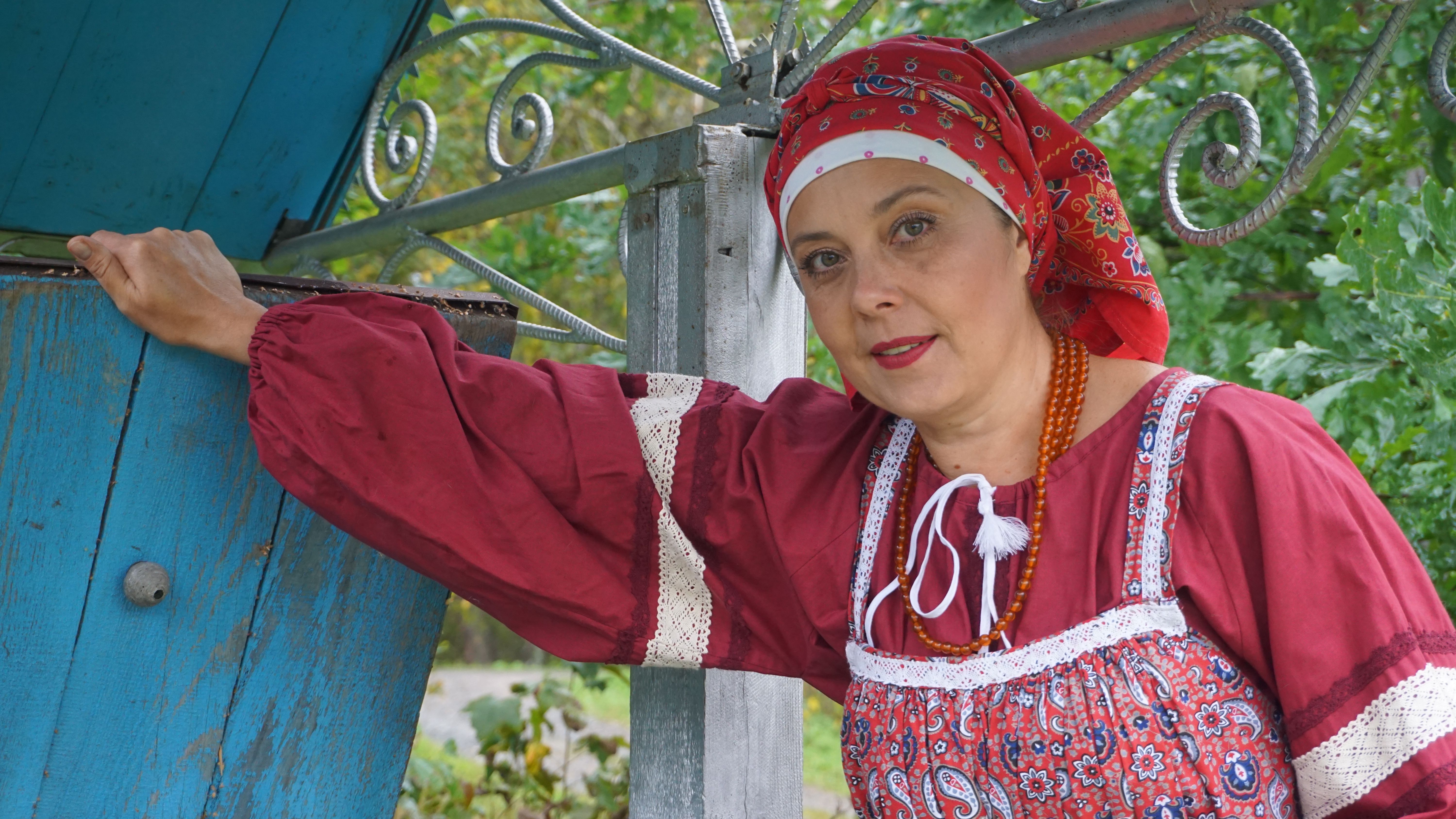 Portrait of a woman in traditional attire standing outdoors by a rustic wooden well.