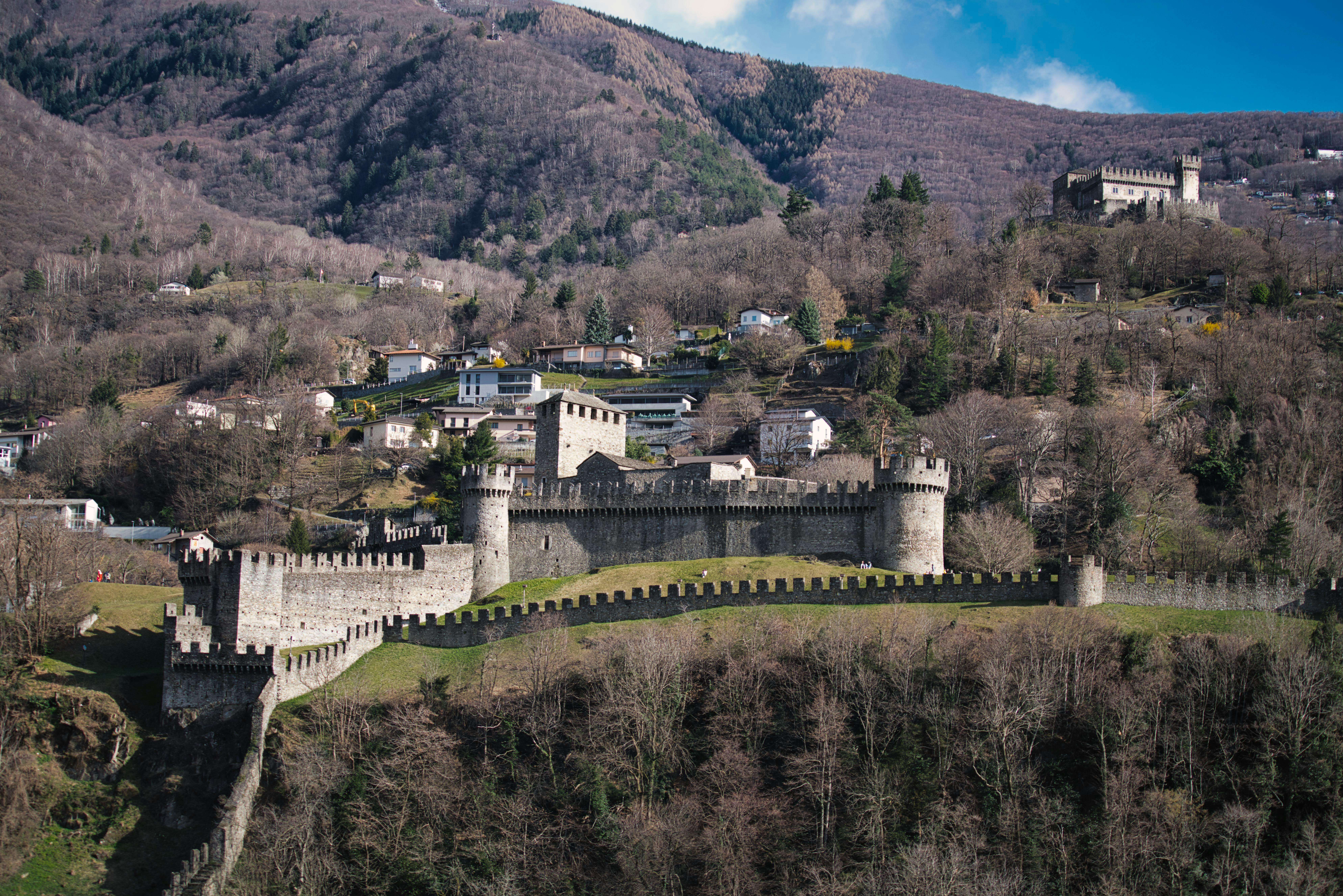 Discover the expansive view of a medieval castle amidst the rolling hills, showcasing historical architecture and lush landscapes. - Bellinzona